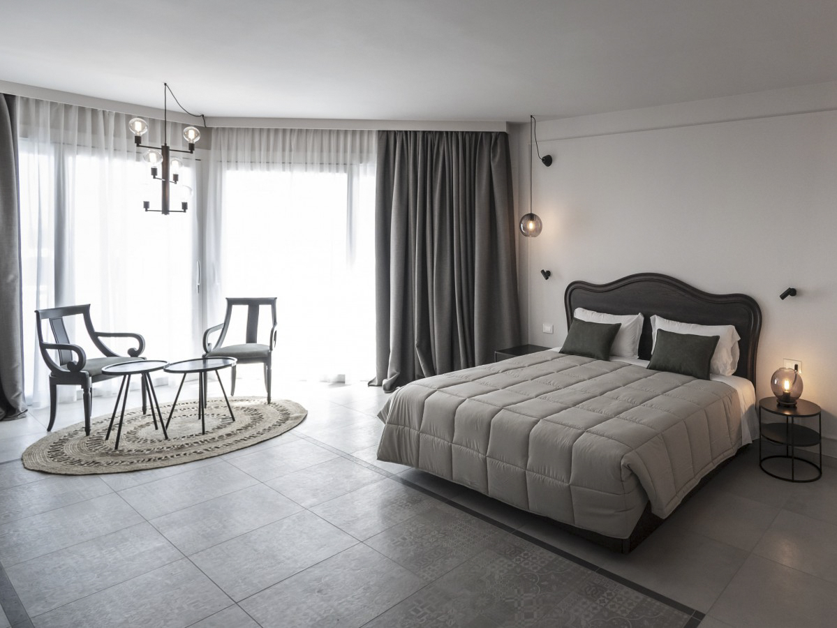 Helles, modernes Schlafzimmer mit Doppelbett, gemütlicher Sitzecke und großen Fenstern. Eleganter, neutraler Stil.