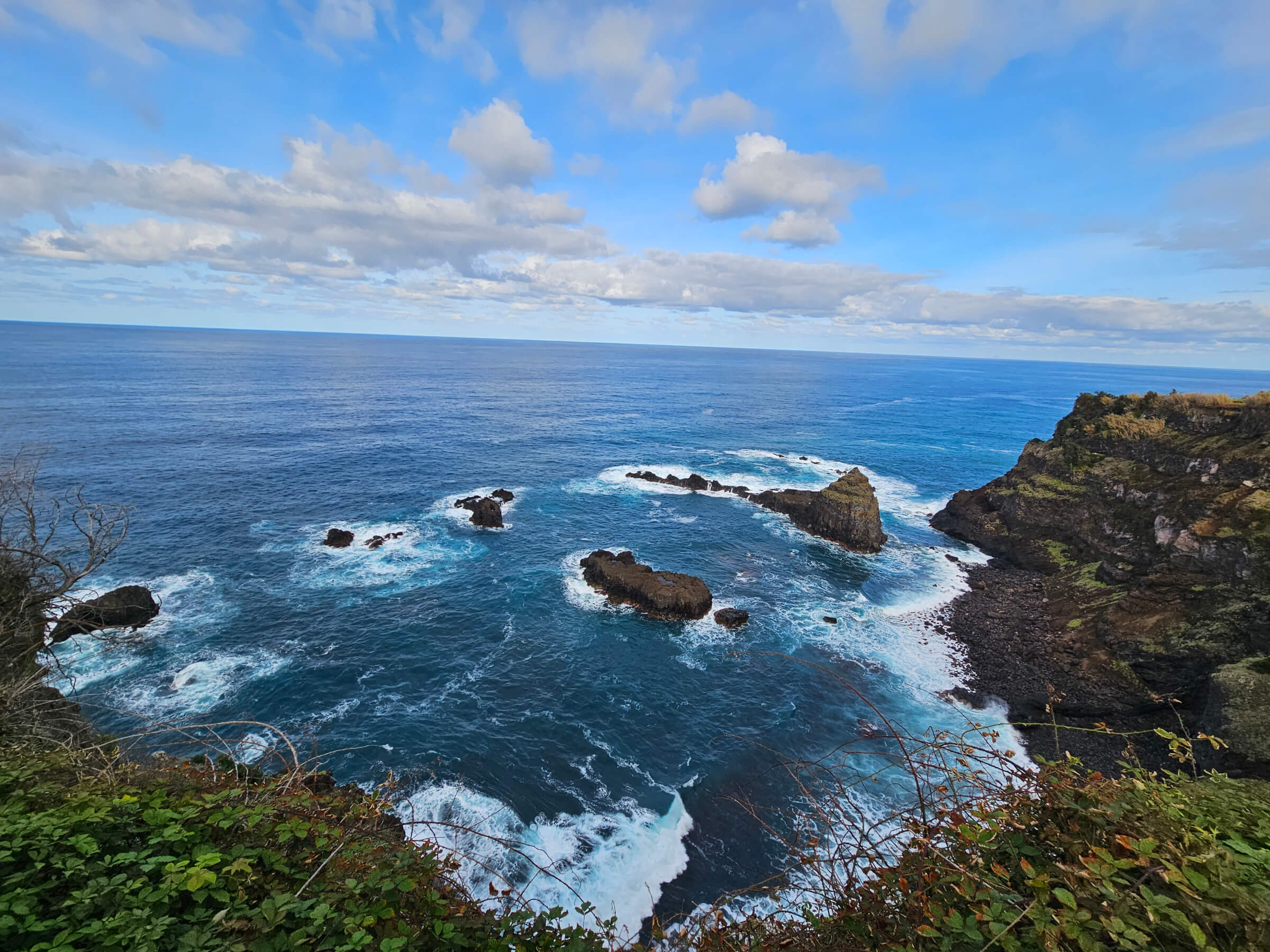 Ein Blick auf den Ozean mit Felsen und Wellen unter einem bewölkten blauen Himmel. Ruhe und Naturschönheit.