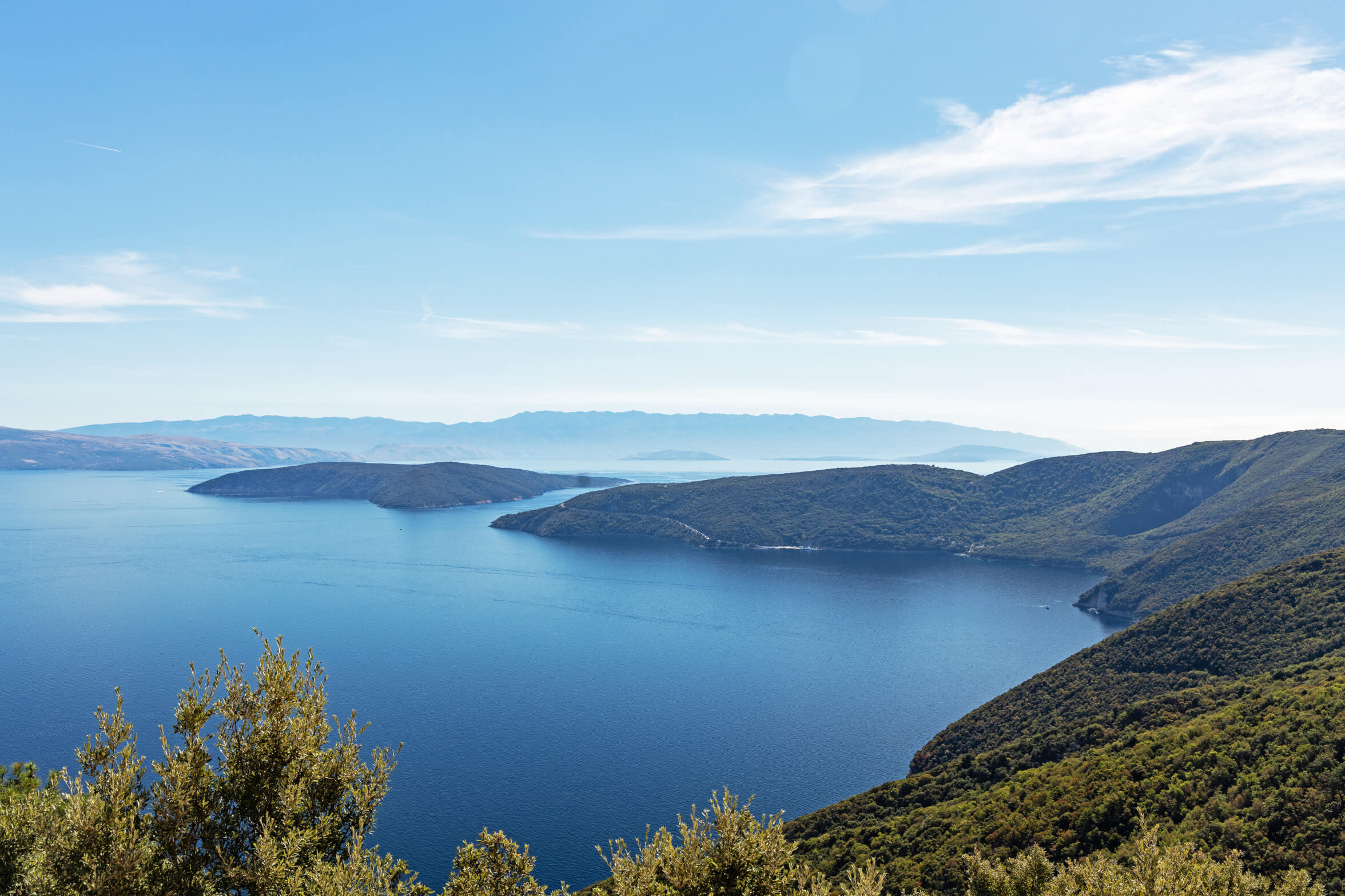 Eine idyllische Küstenlandschaft mit Inseln im blauen Wasser und sanften Hügeln unter klarem Himmel.