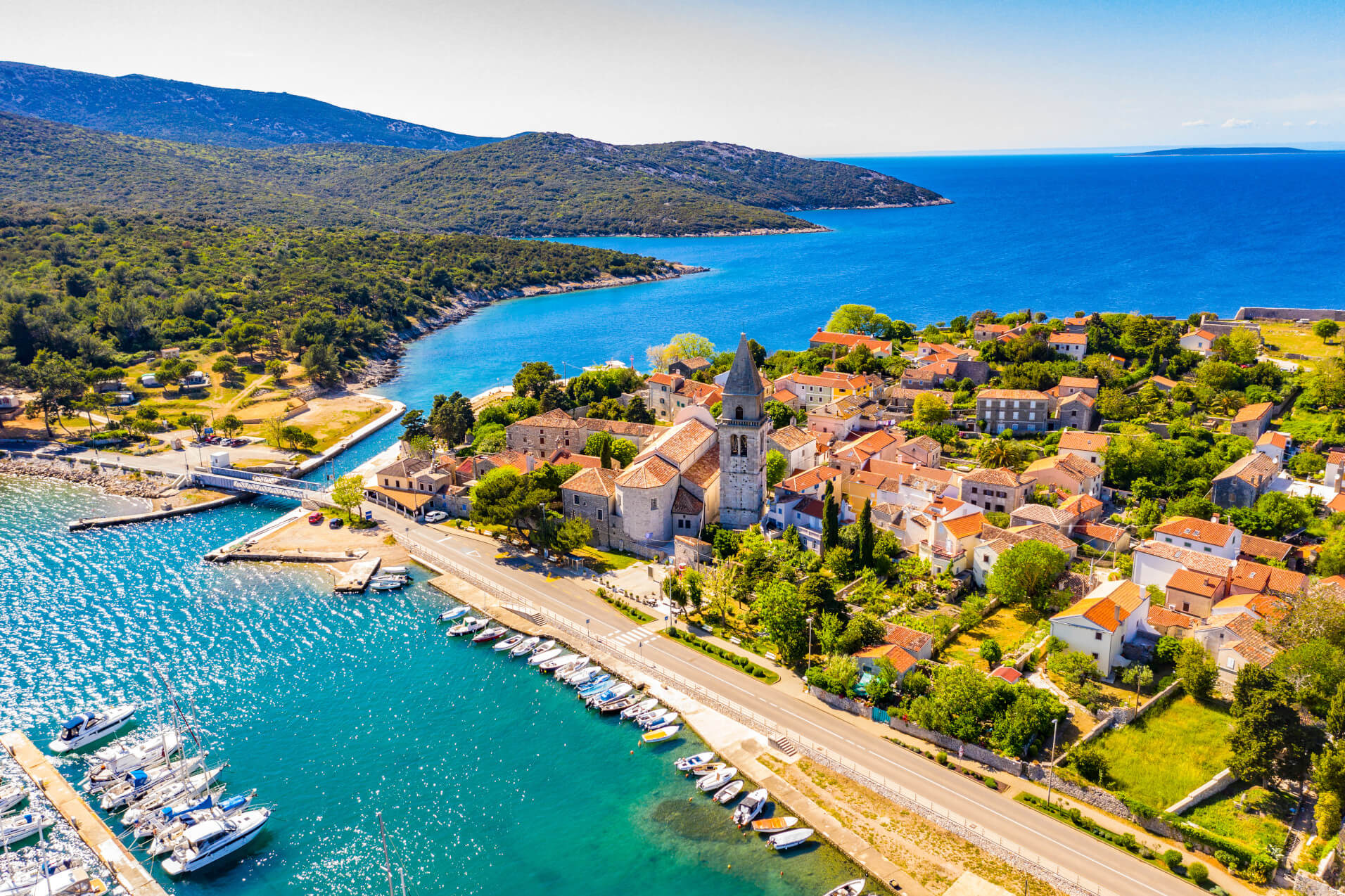 Ein malerisches Küstendorf mit einem Hafen, blauer See und sanften Hügeln im Hintergrund.