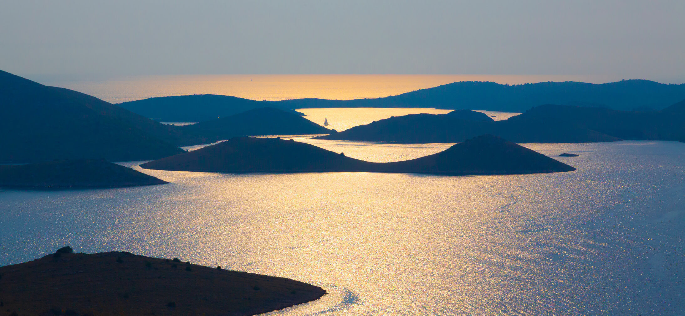 Eine malerische Landschaft mit sanften Hügeln und glitzerndem Wasser bei Sonnenuntergang.