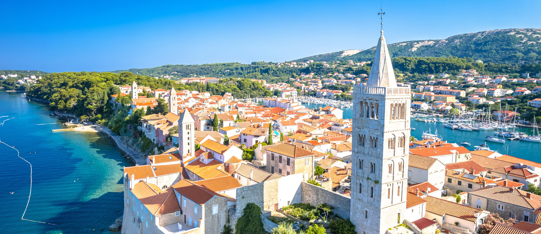 Eine malerische Küstenstadt mit roten Dächern, grünen Hügeln und einem hafen, umgeben von klarem Wasser.