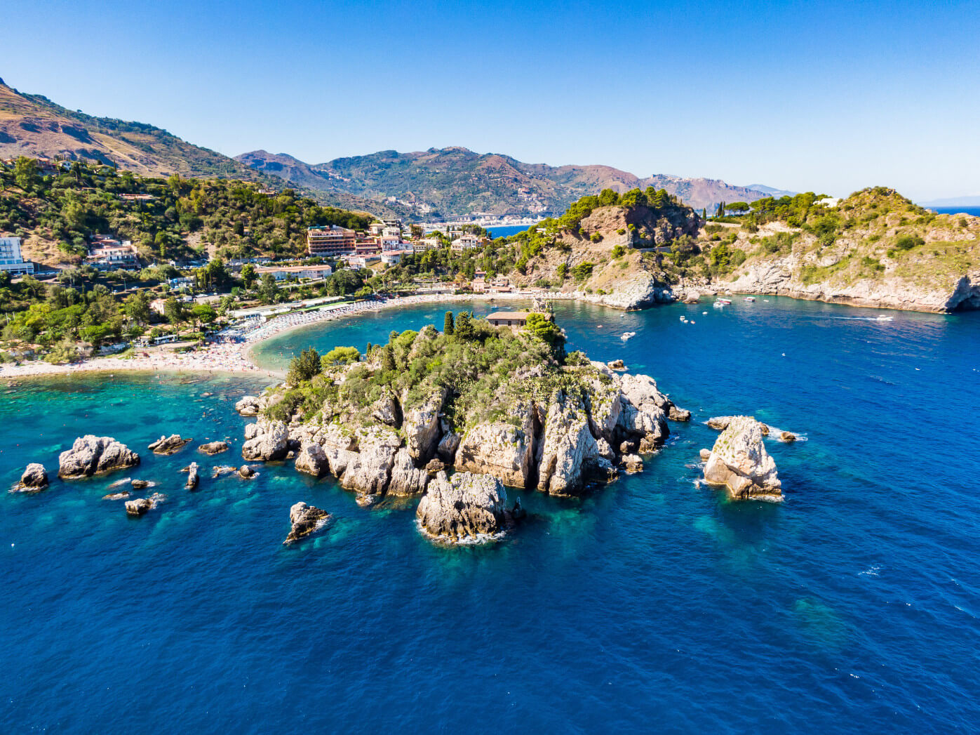 Eine malerische Küstenlandschaft mit klarem Wasser, Stränden und bewaldeten Hügeln im Hintergrund.