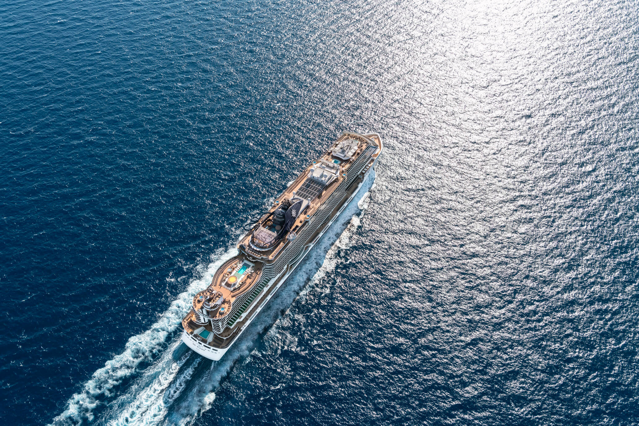 Ein großes Kreuzfahrtschiff fährt über das blaue Wasser, die Sonne spiegelt sich auf der Oberfläche.