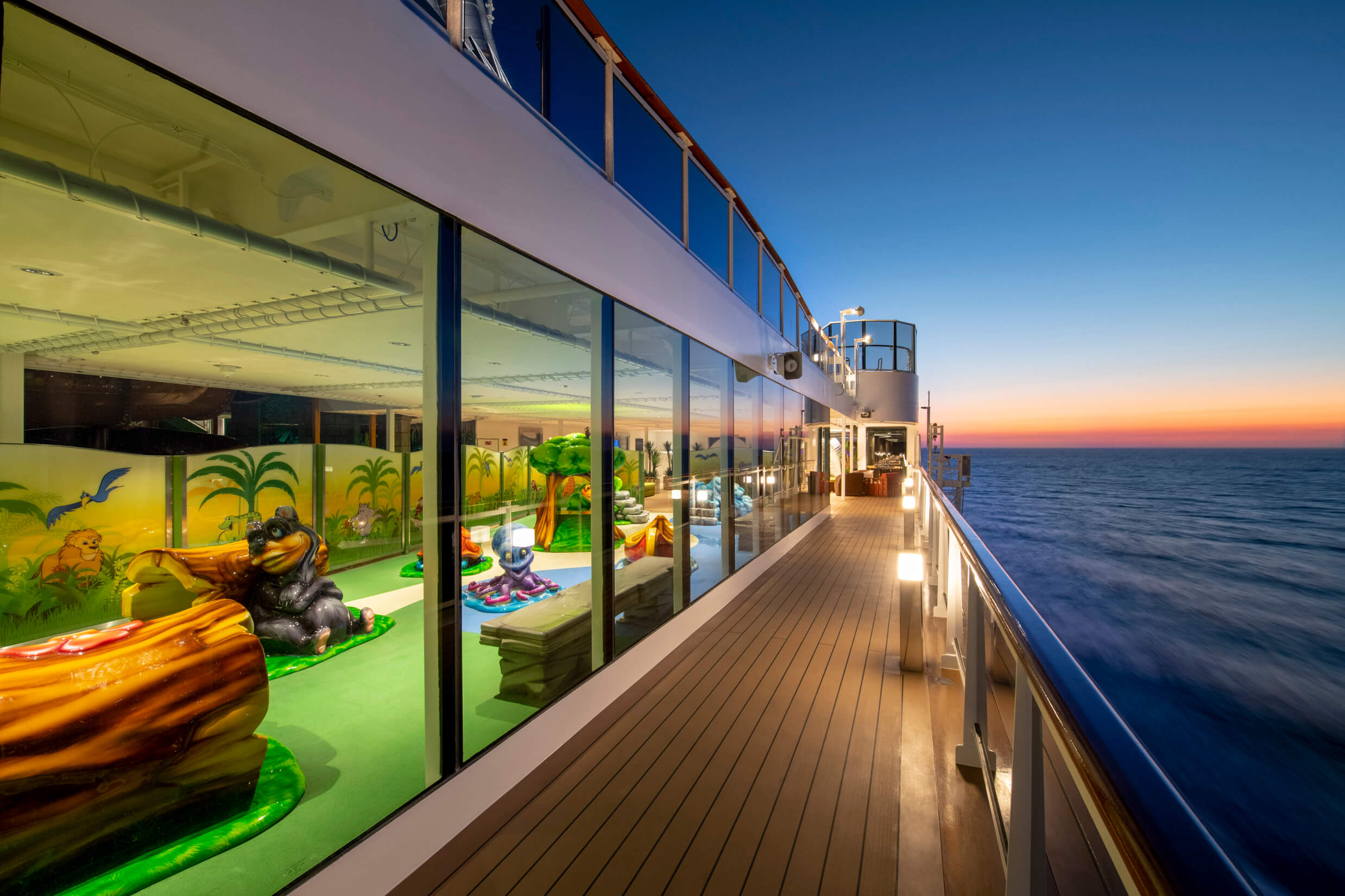 Ein Kreuzfahrtschiff bei Sonnenuntergang, mit Spielbereich und Blick auf das Meer. Leuchtende Farben und entspannte Atmosphäre.