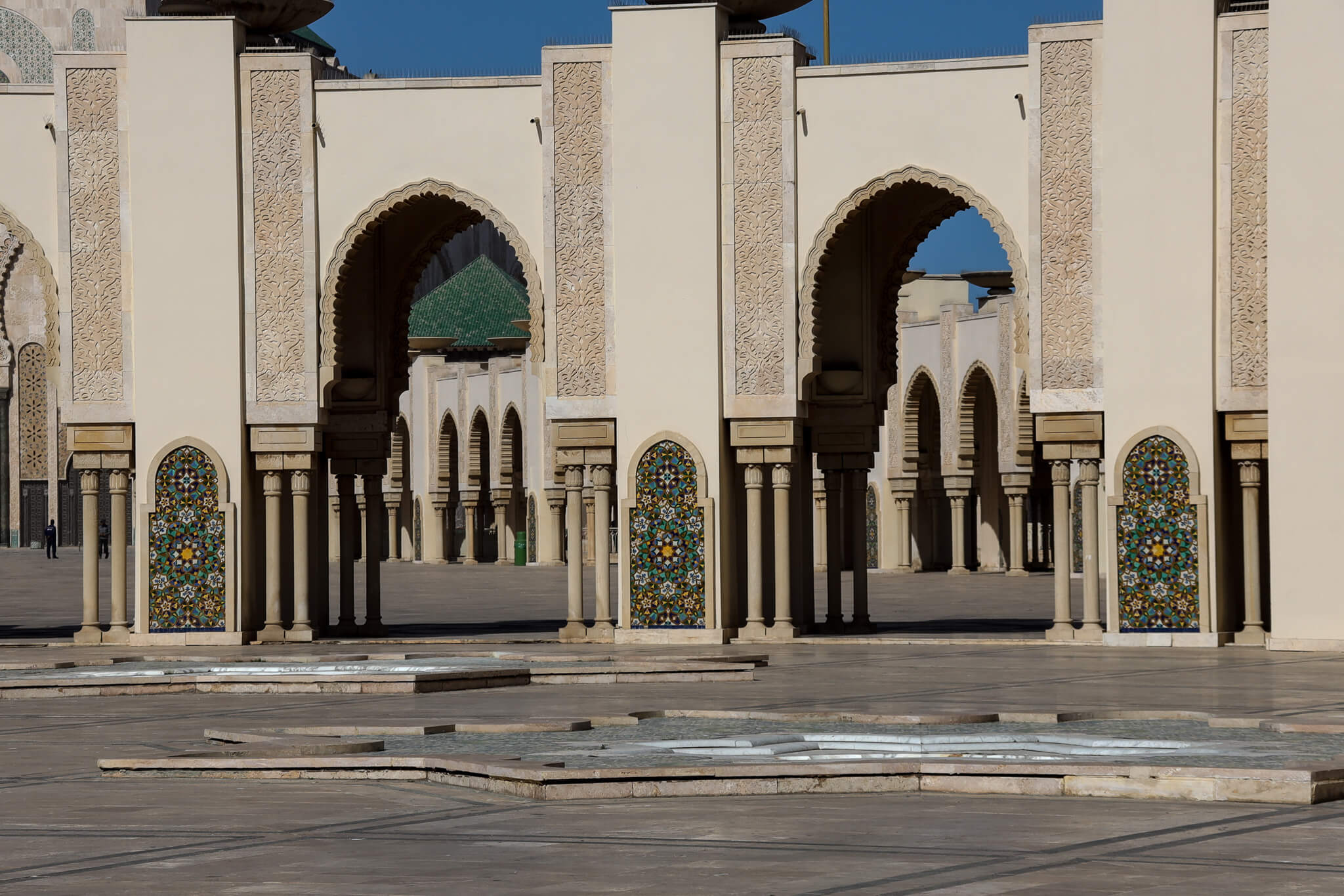 Eine zauberhafte architektonische Struktur mit Bögen und bunten Fliesen, umgeben von leerem Platz. Draußen blauer Himmel.