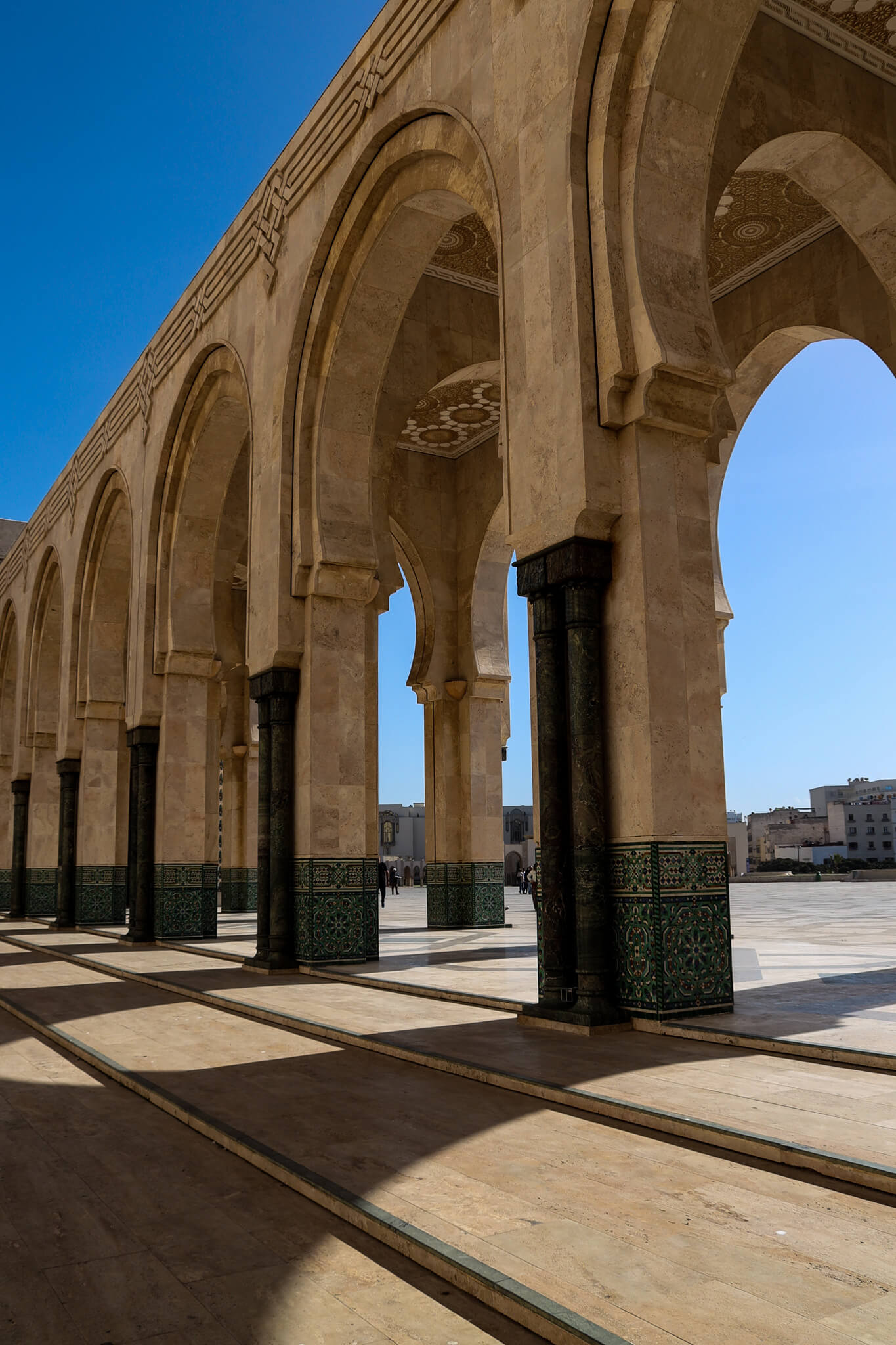 Ein architektonischer Innenhof mit hohen Bögen, dekorierten Säulen und klarem blauen Himmel im Hintergrund.
