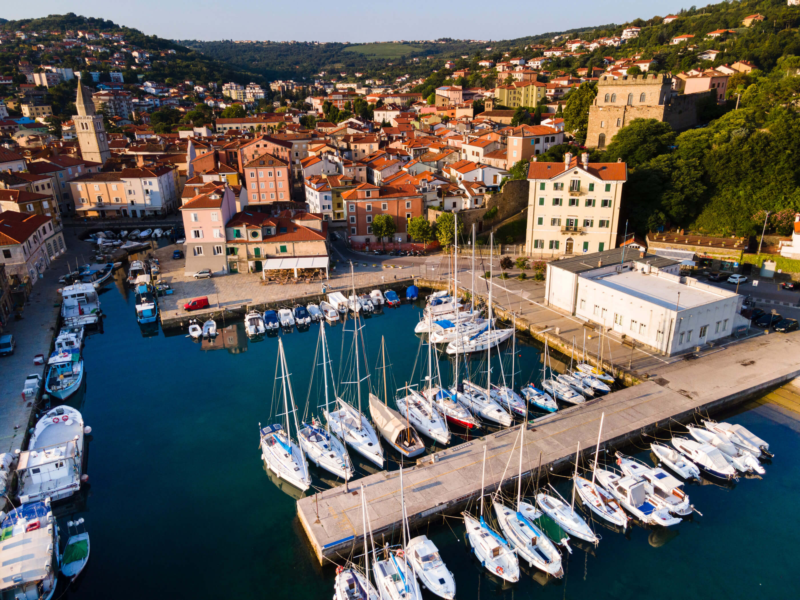 Eine malerische Hafenansicht mit Booten und bunten Häusern im Hintergrund, umgeben von grünen Hügeln.