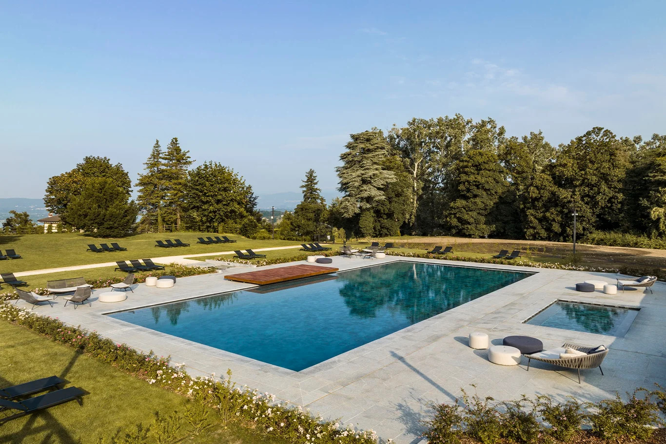 Eleganter Pool mit Liegen in einer grünen Landschaft, umgeben von Bäumen und klarem Himmel. Entspannung pur!