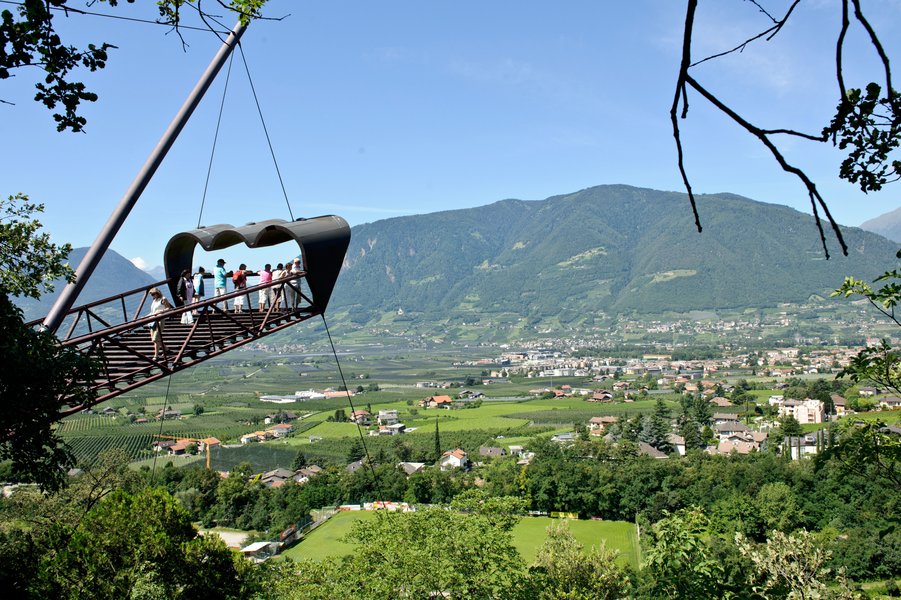Eine schwebende Aussichtsplattform bietet einen atemberaubenden Blick auf das grüne Tal und die umliegenden Berge.