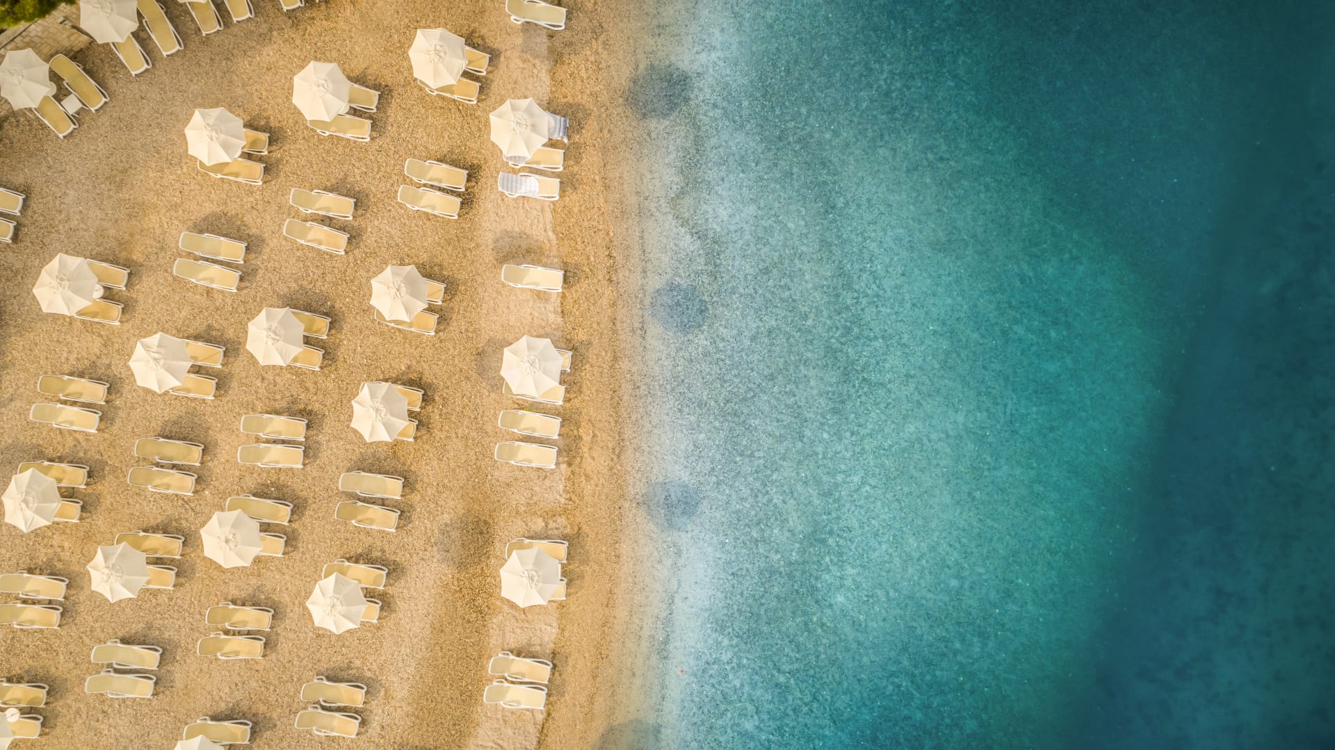 Ein Strandbild mit Liegen und Sonnenschirmen, die das türkisfarbene Wasser und den Sand umrahmen.