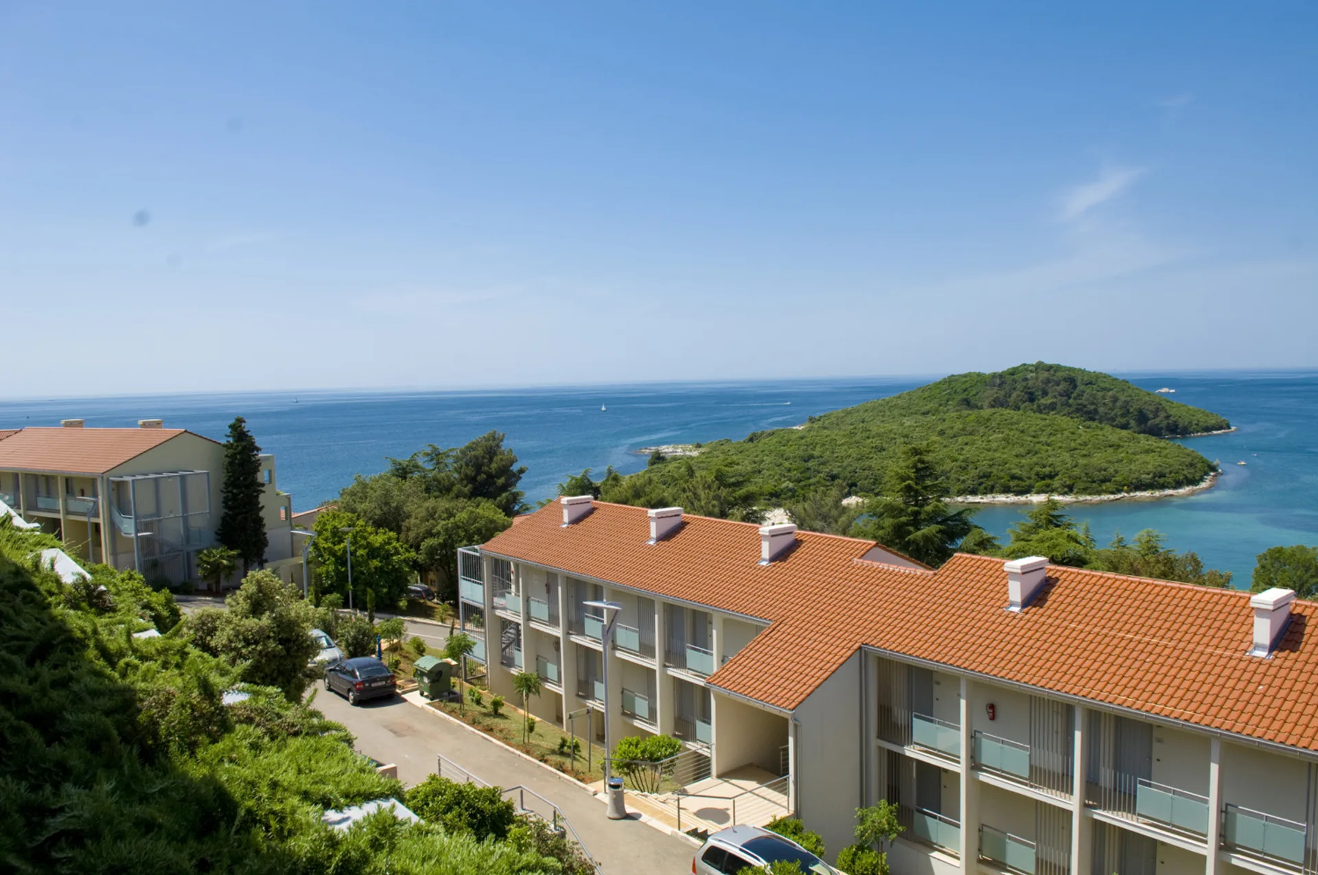 Blick auf das Meer mit grüner Insel und schönen Wohngebäuden, umgeben von Bäumen und klarem blauen Himmel.