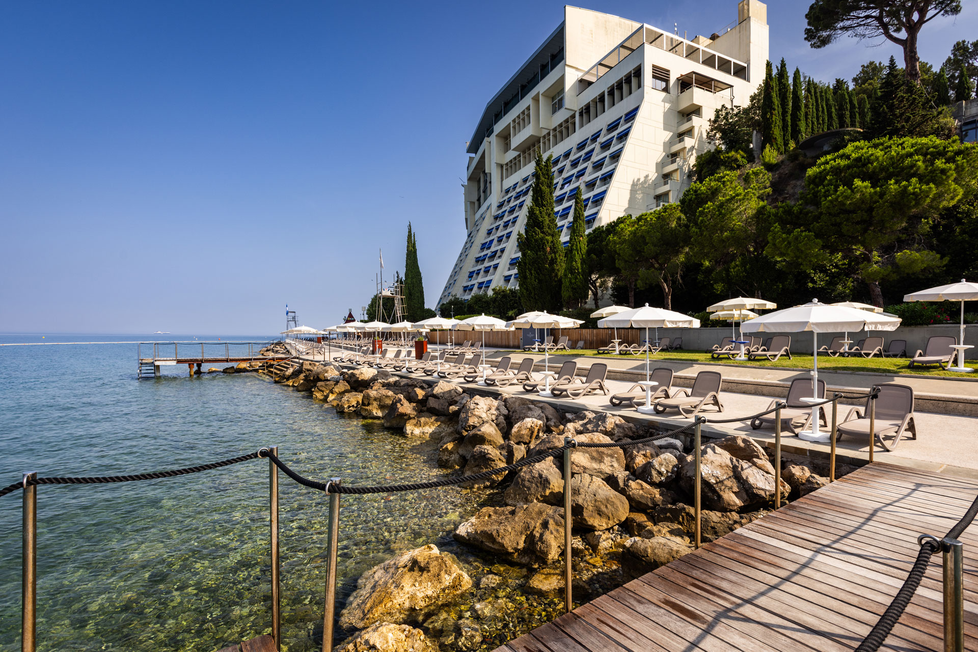 Ein modernes Hotel am Wasser mit Liegen, Sonnenschirmen und einem schönen Steg entlang der Küste.