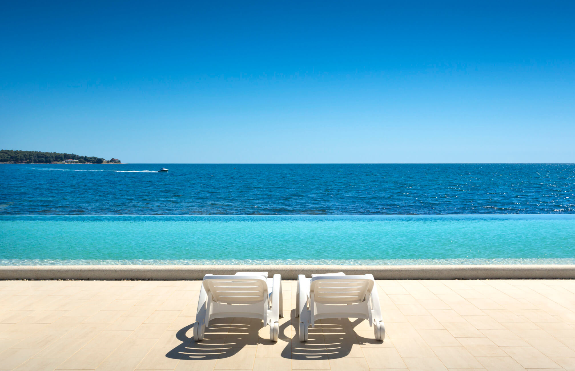 Schöne Aussicht auf den Ozean mit Liegestühlen am Rand eines Infinity-Pools unter strahlend blauem Himmel.