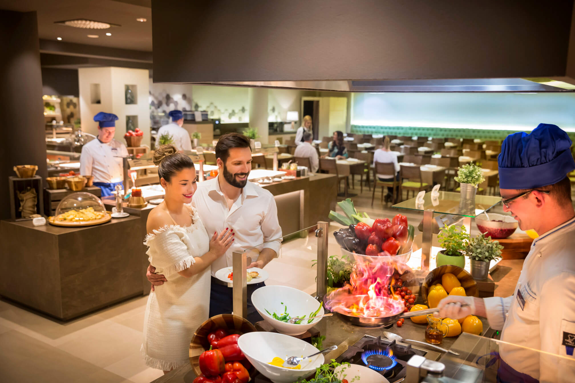 Ein Paar genießt ein Essen in einem Restaurant, während ein Koch leidenschaftlich am Herd kocht.
