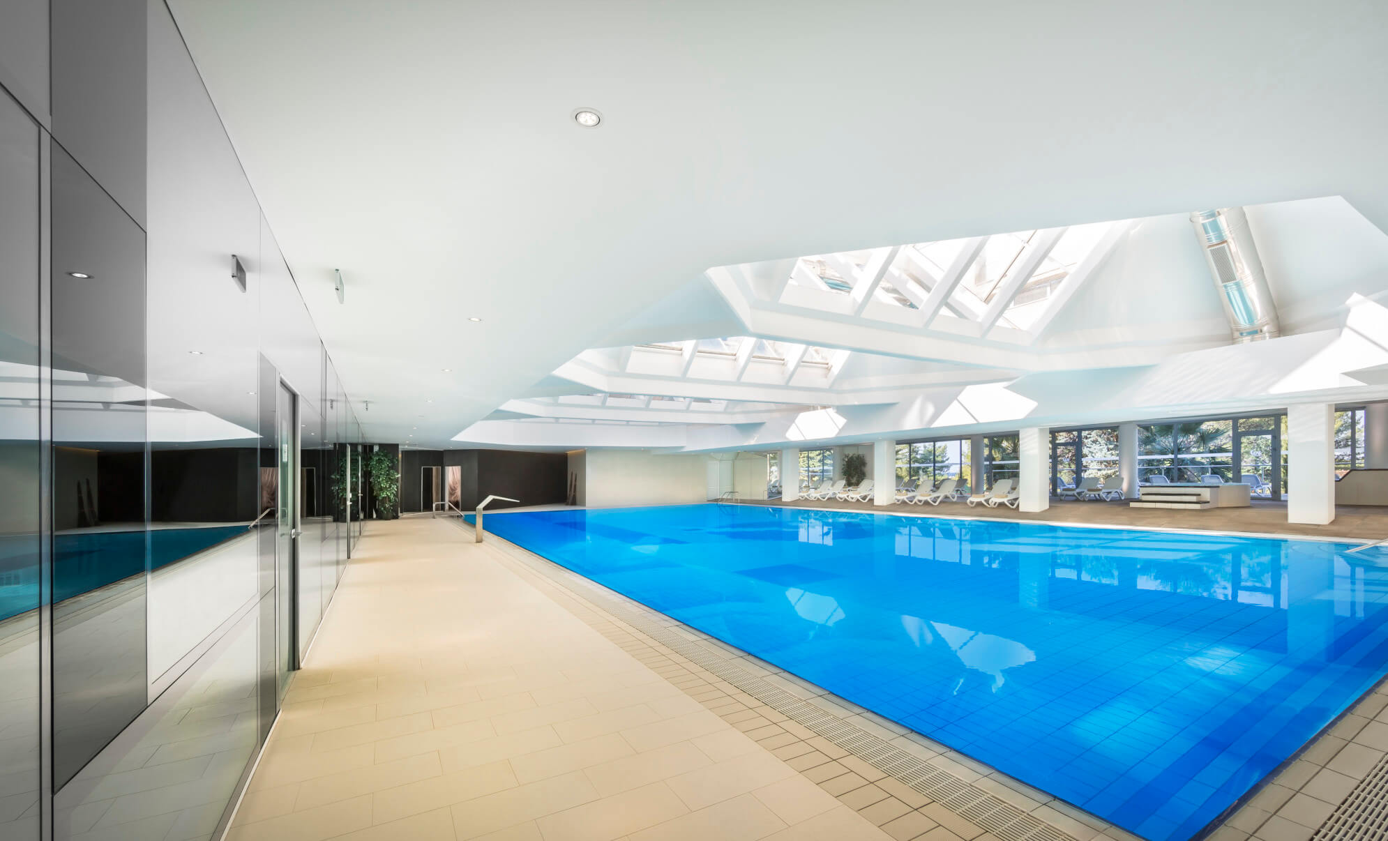 Ein modernes Hallenbad mit großem blauem Wasserbecken, lichtdurchfluteten Fenstern und eleganter Architektur.