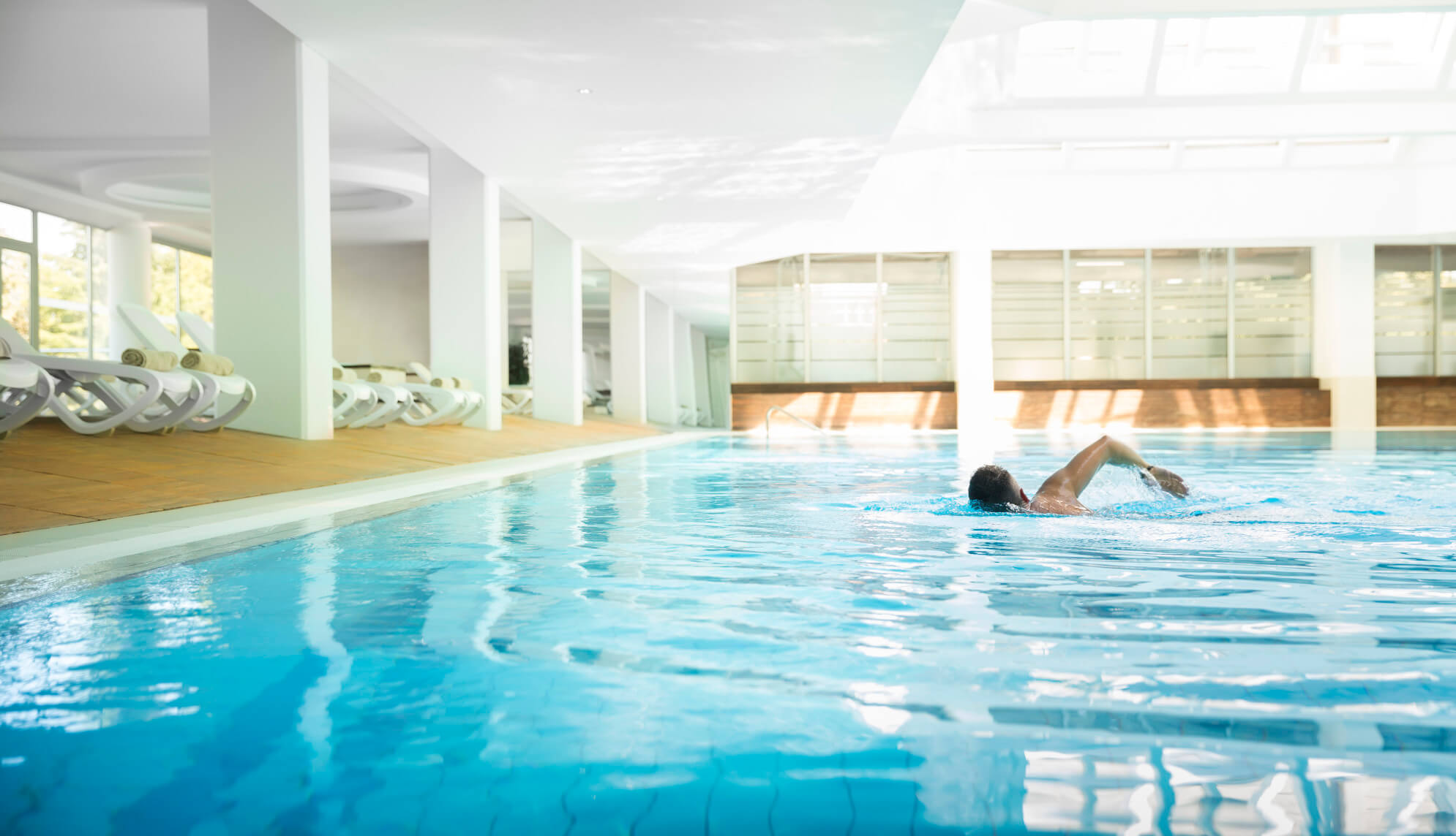 Ein strukturierter Innenpool mit einem Schwimmer und Liegen im Hintergrund, umgeben von natürlichem Licht.
