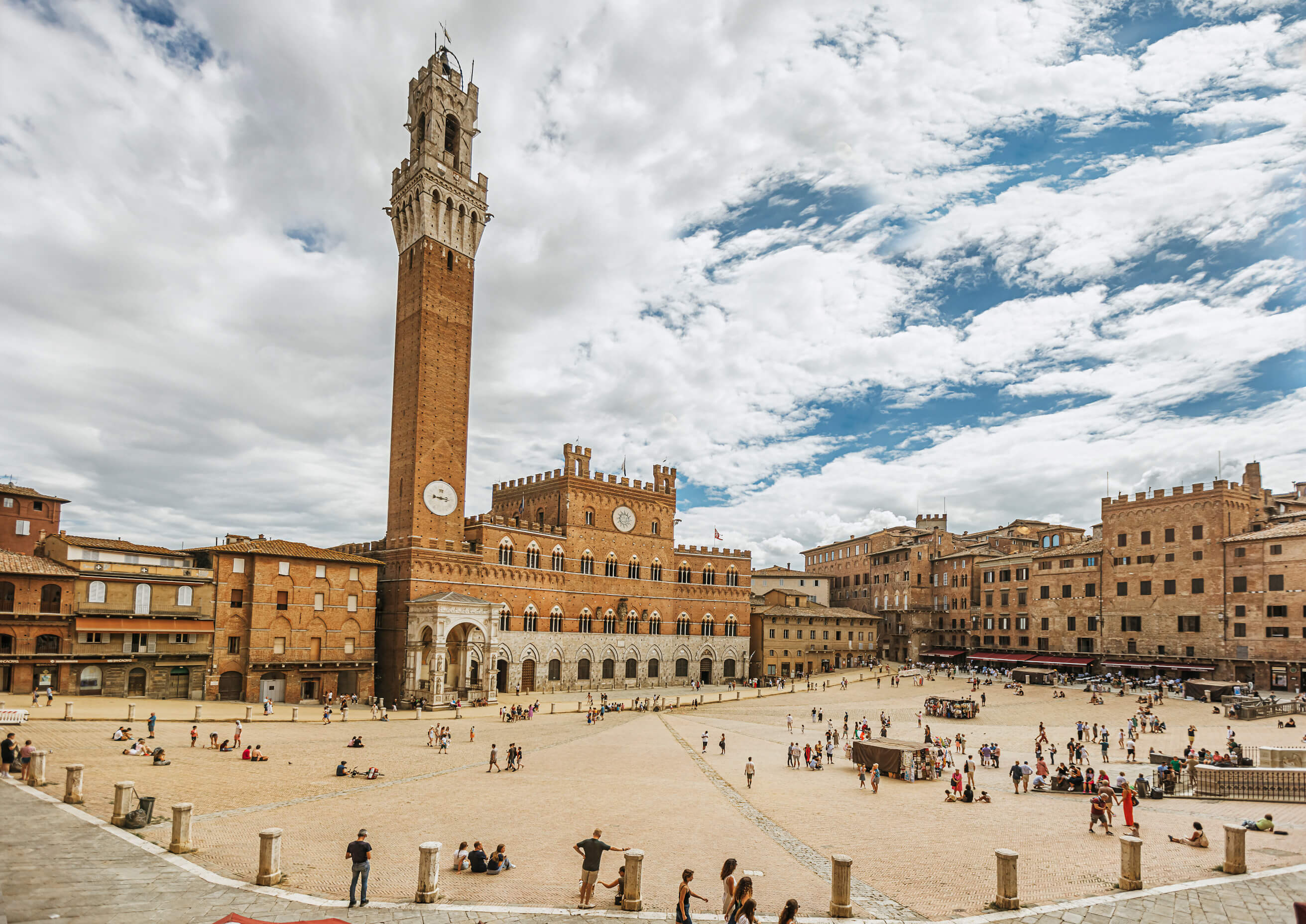 Der Platz in Siena mit dem hohen Turm im Hintergrund und vielen Menschen unter einem bewölkten Himmel.