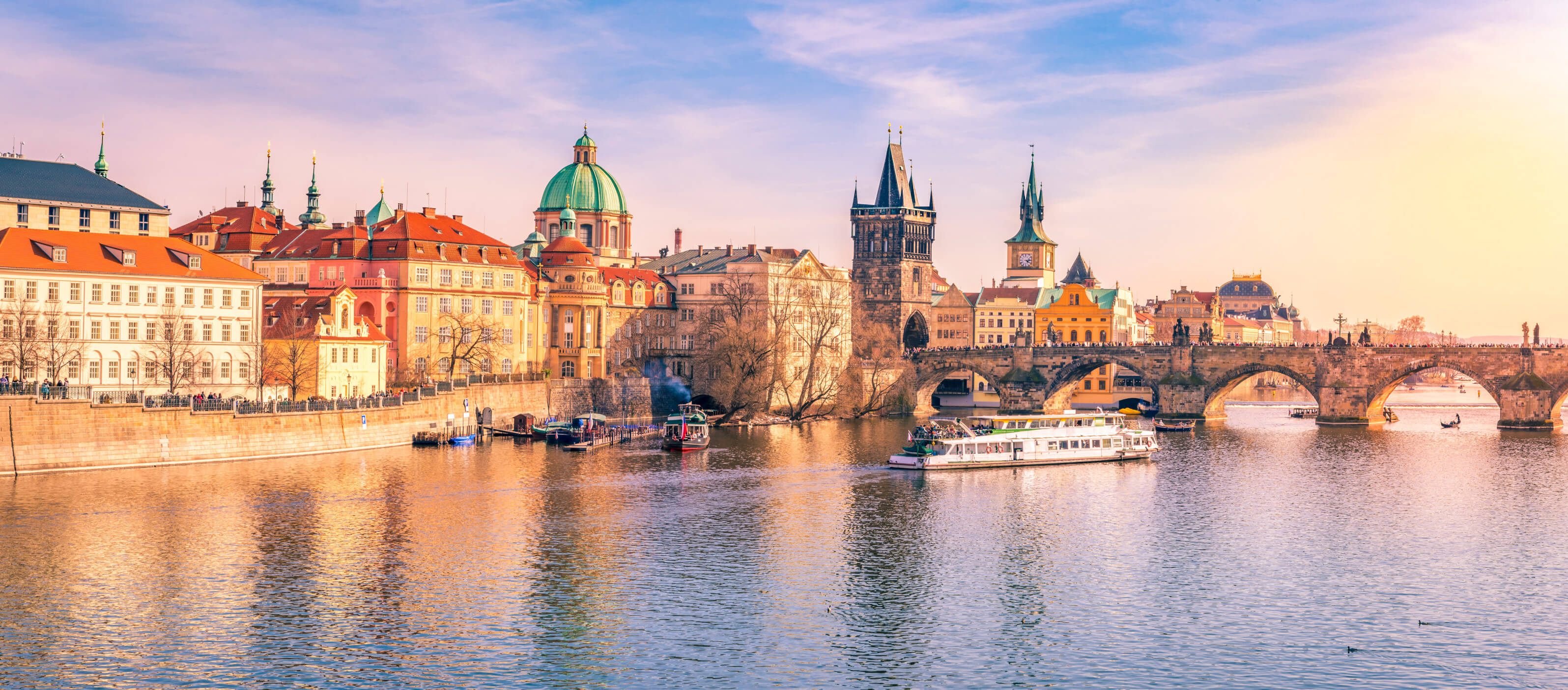 Die Karlsbrücke und die malerische Architektur Prags spiegeln sich im ruhigen Wasser. Ein Boot fährt vorbei.