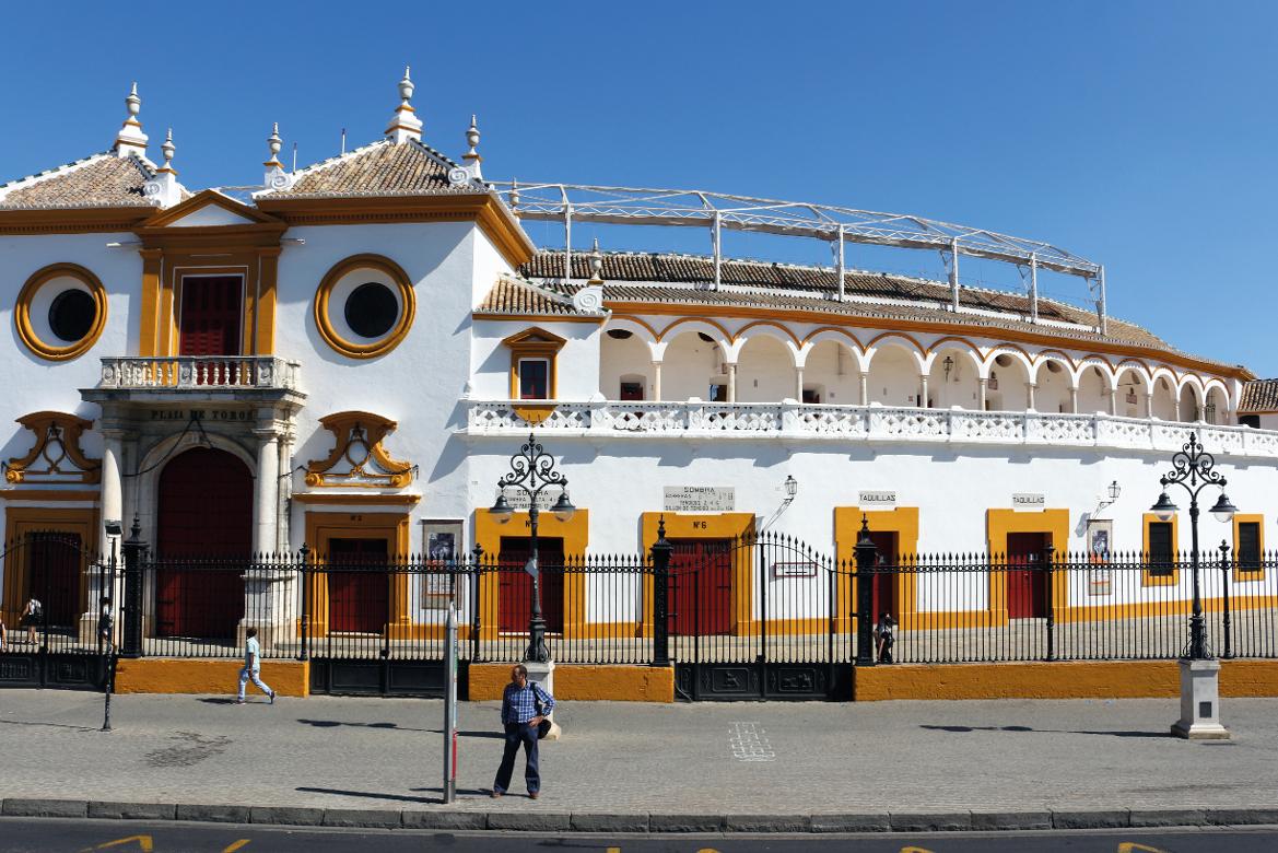 Eine historische Arena mit weißen und gelben Akzenten, umgeben von einem klaren blauen Himmel und Menschen.