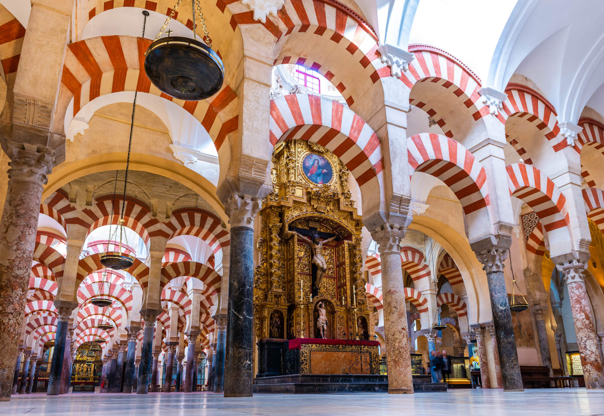 Eine beeindruckende Hallenkirche mit rot-weißen Bögen und einer prunkvollen goldenen Altarwand.
