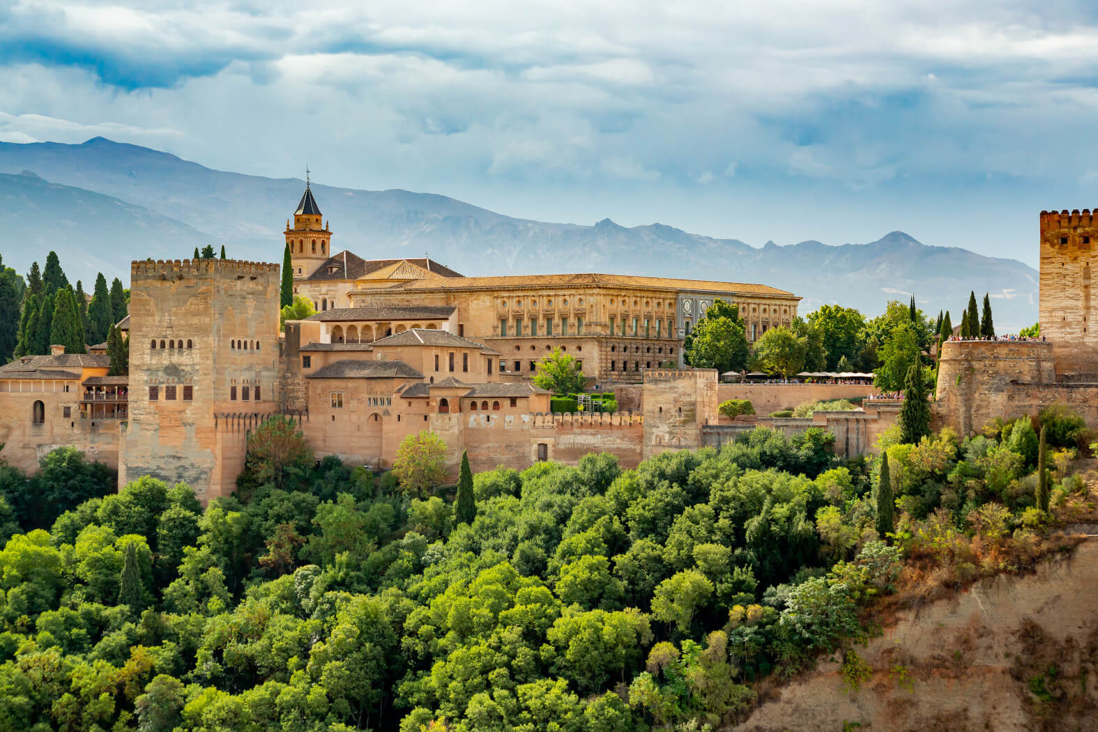 Die Alhambra in Granada, umgeben von grünen Bäumen und Bergen, strahlt majestätische Schönheit aus.