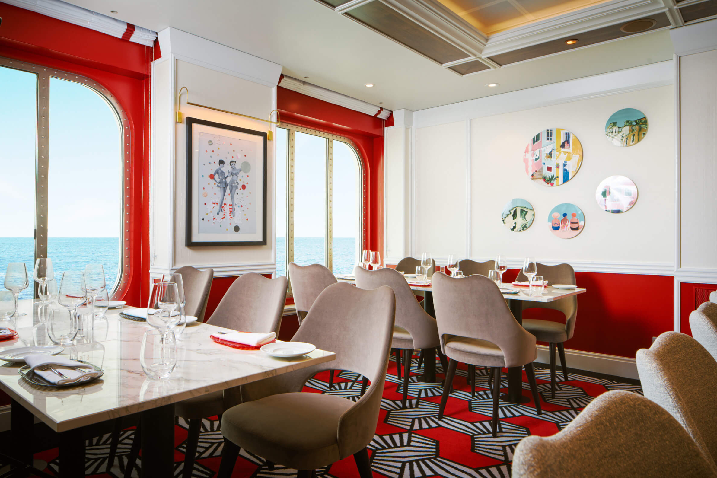 Elegantes Restaurant mit Meerblick, roter Wandfarbe und stilvollen Möbeln, dekoriert mit Kunstwerken.