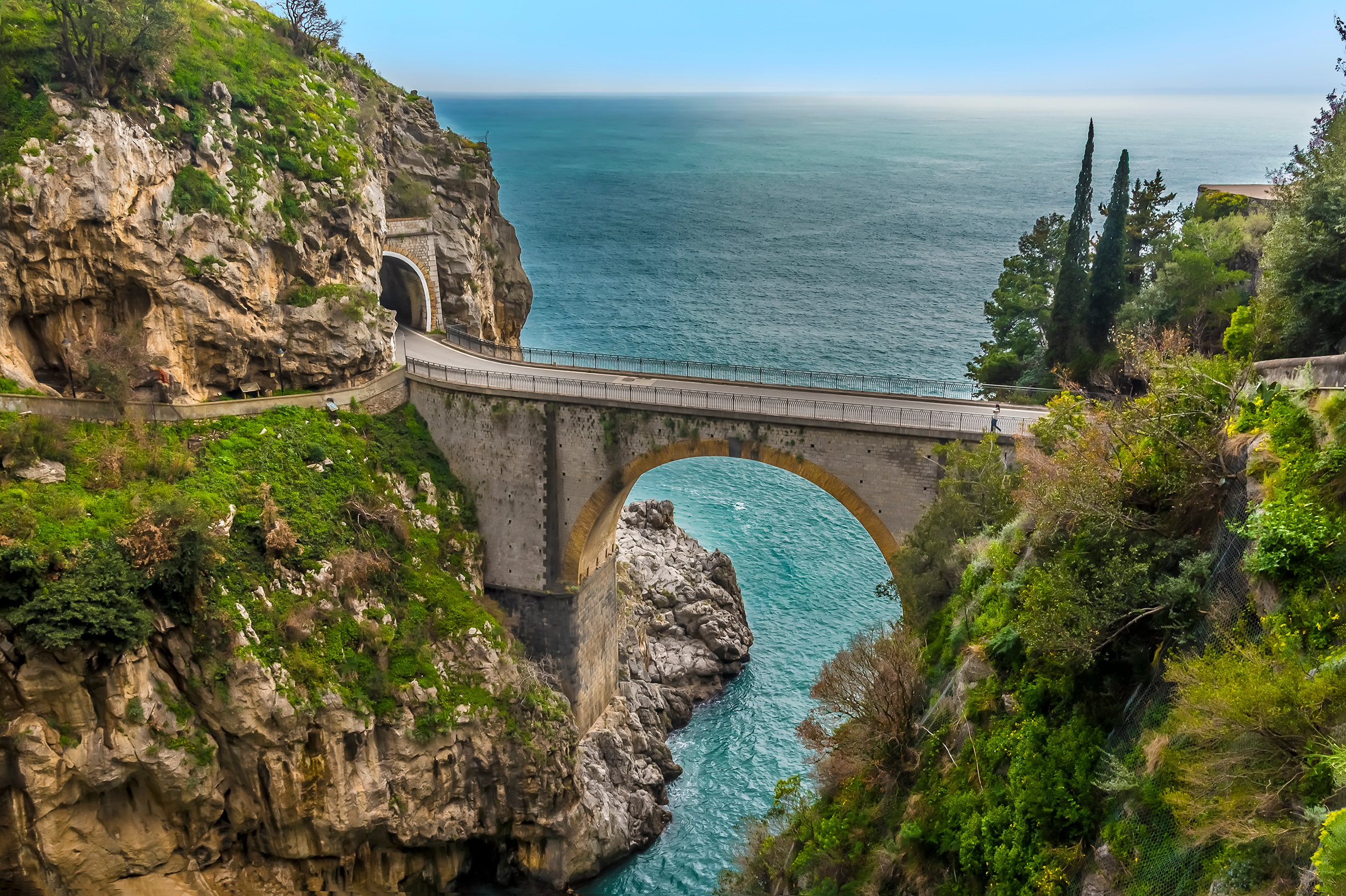 Eine beeindruckende Brücke über turquoise Wasser, umgeben von grünen Klippen und einer Küstenlandschaft.
