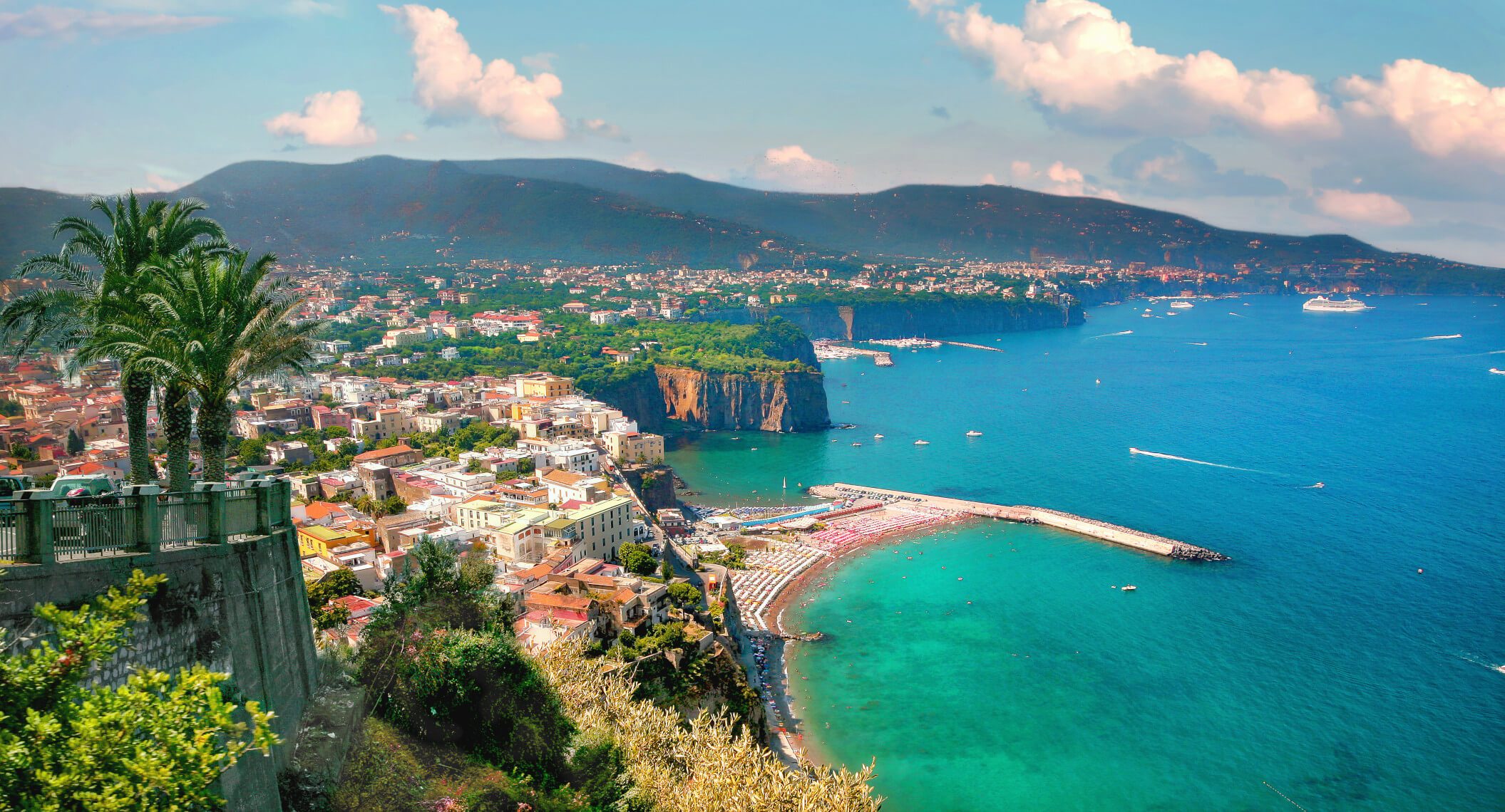 Blick auf eine Küstenstadt mit Palmen, Stränden und blauem Wasser, umgeben von Bergen und einer malerischen Landschaft.