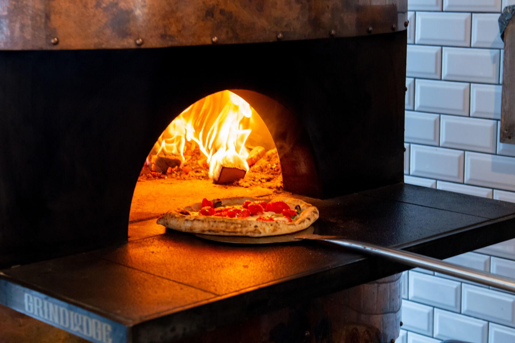 Ein Pizzaofen mit Flammen, in dem eine Pizza mit Tomaten und Kräutern gebacken wird.