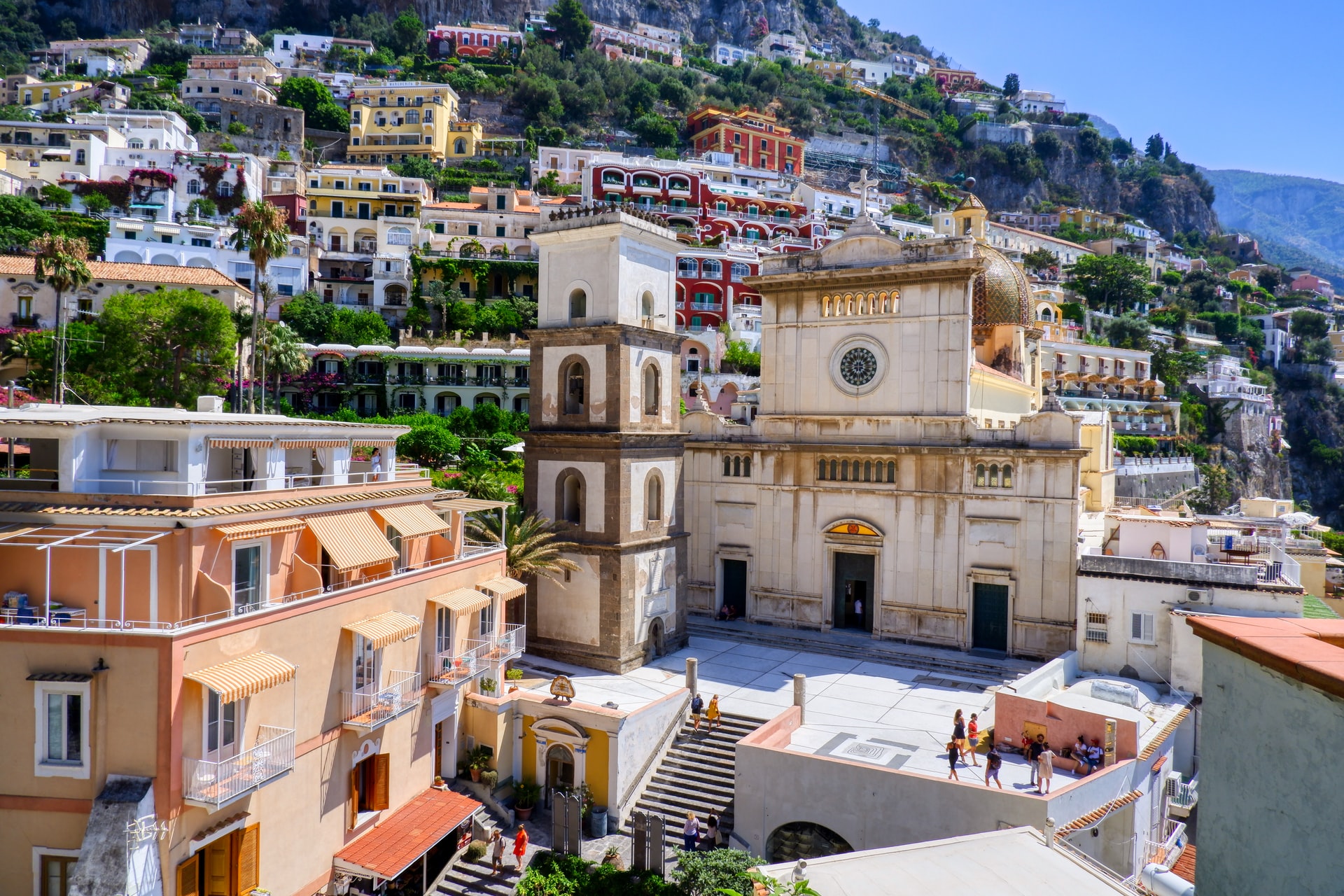 Bunte Gebäude in Positano, Italien, mit einer markanten Kirche und terrassierten Hügeln im Hintergrund.