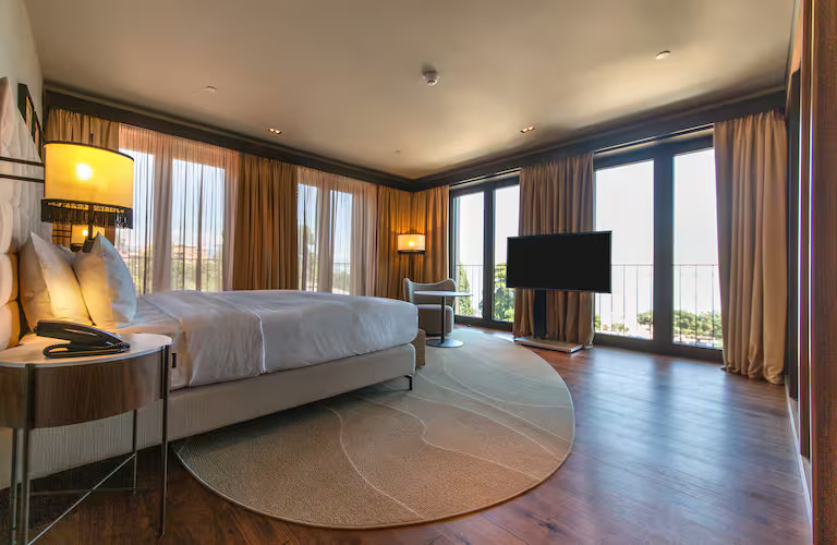 Helles, modernes Hotelzimmer mit einem Bett, Fernseher und großen Fenstern für viel Tageslicht.