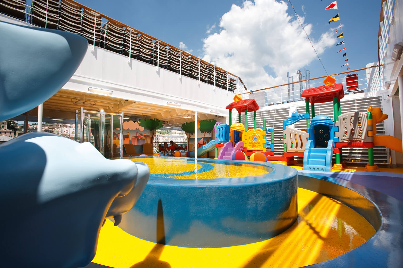 Ein bunter Spielbereich auf einem Schiff mit Wasserfontäne und verschiedenen Spielgeräten im Freien.