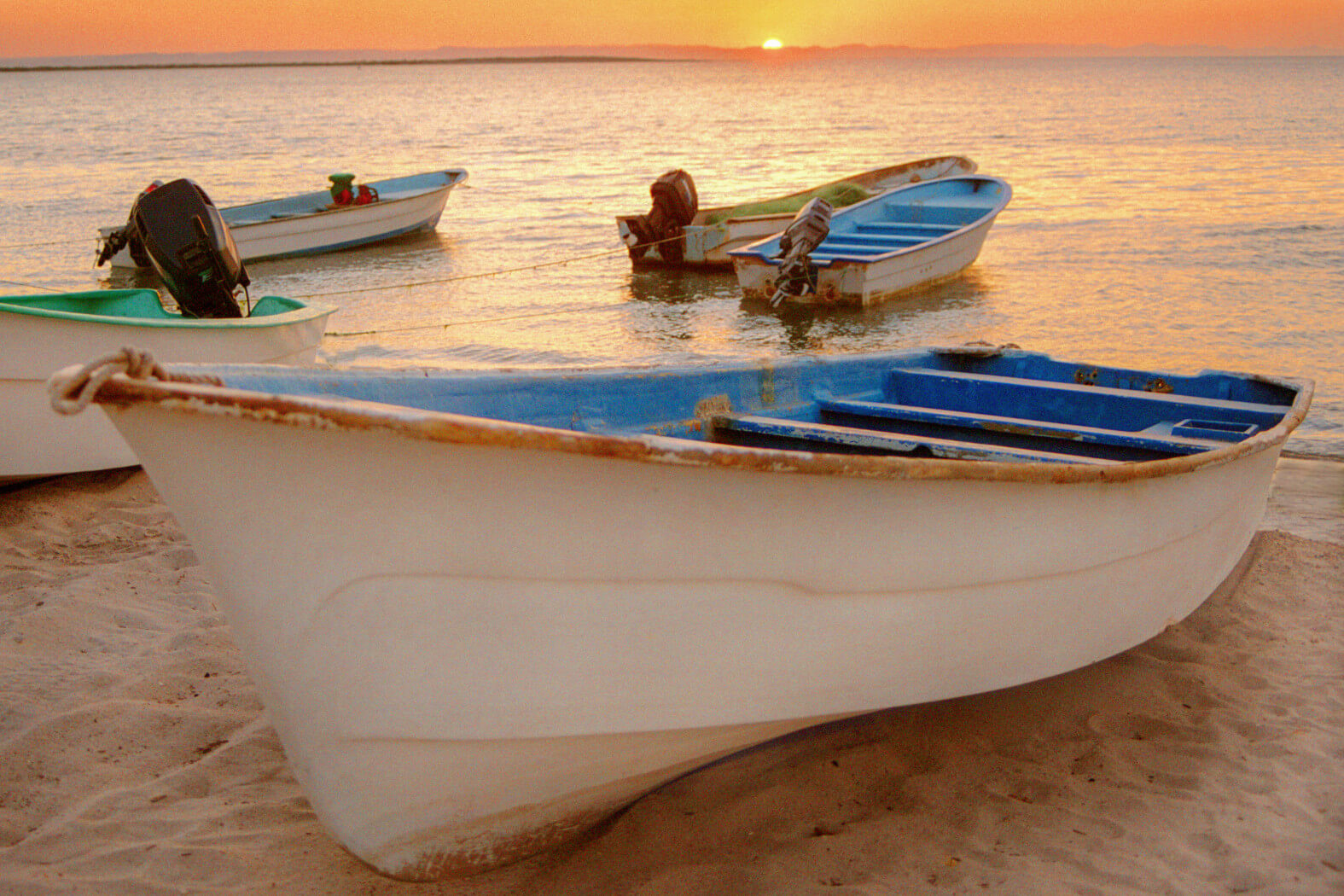 Boote stehen am Ufer, während die Sonne am Horizont untergeht und das Wasser sanft glitzert.