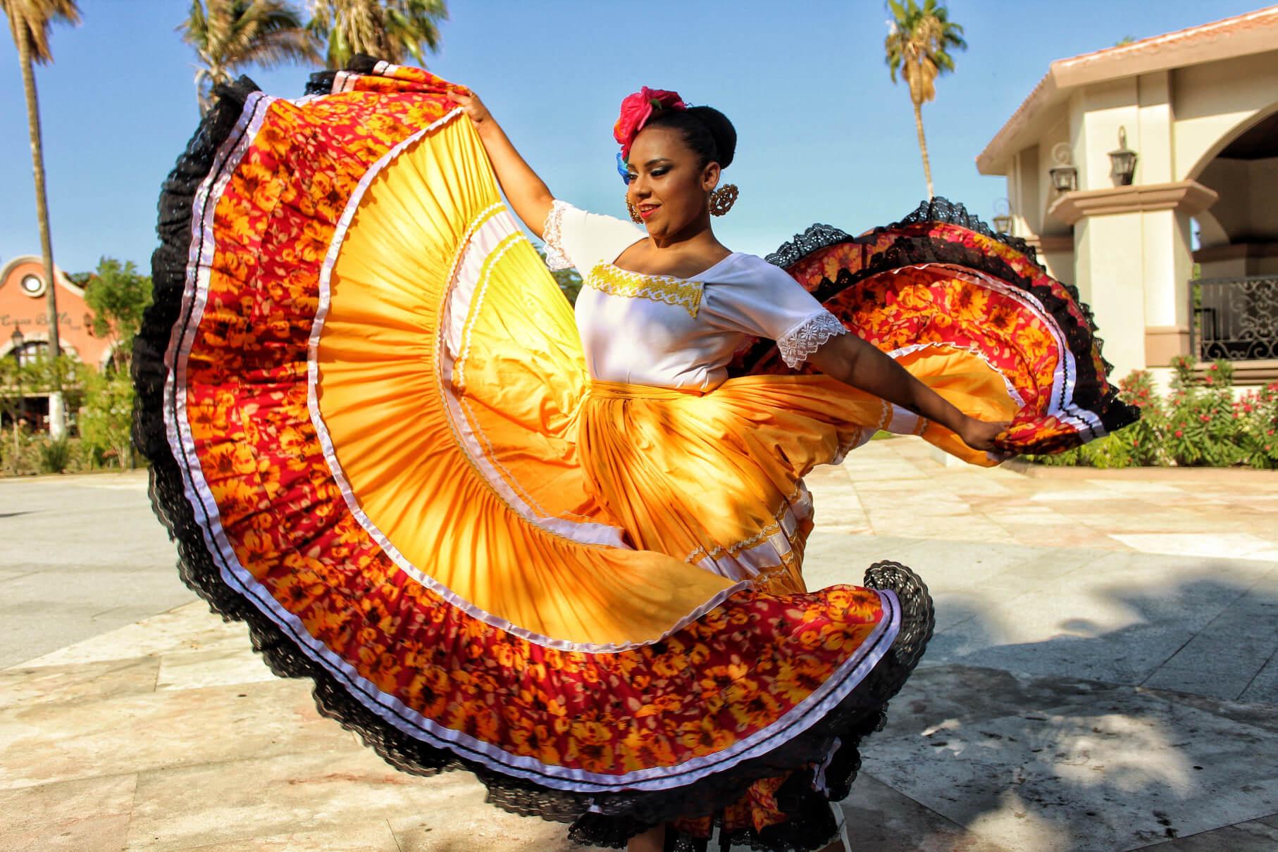 Eine Tänzerin in buntem Kleid schwingt ihren Rock vor einer tropischen Kulisse.