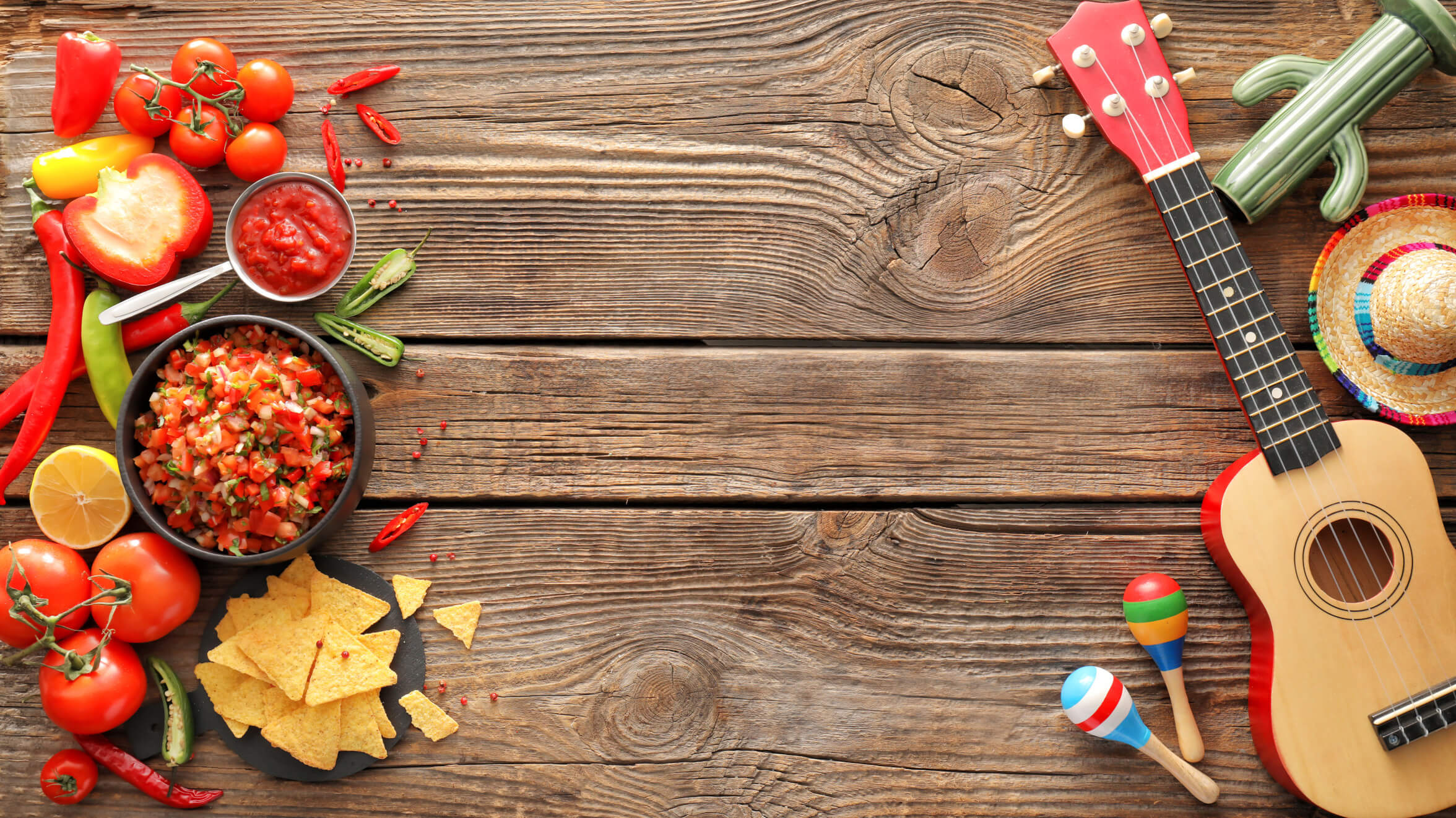 Bunte Zutaten für Salsa, Tortilla-Chips und eine Ukulele auf rustikalem Holz; festliche Stimmung.