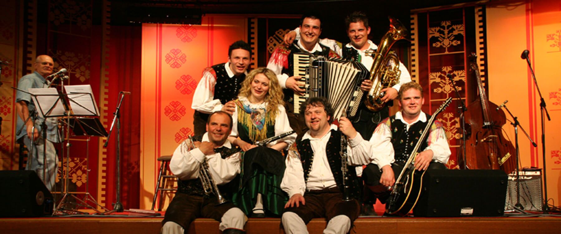 Eine fröhliche Musikergruppe posiert mit Instrumenten auf einer bunten Bühne bei einer Live-Performance.