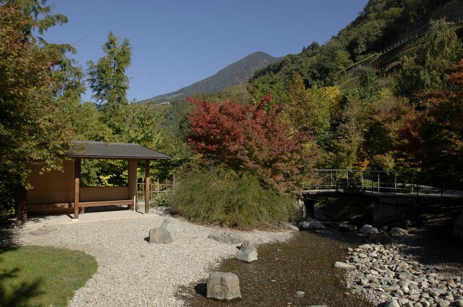 Ein ruhiger Ort mit einem Bach, bunten Bäumen und einer kleinen Hütte inmitten von Bergen.