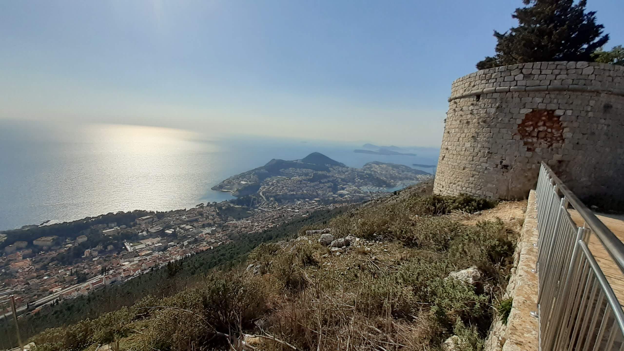 Blick auf das Meer und die Stadt von einer Bergspitze mit einem historischen Steinturm im Vordergrund.