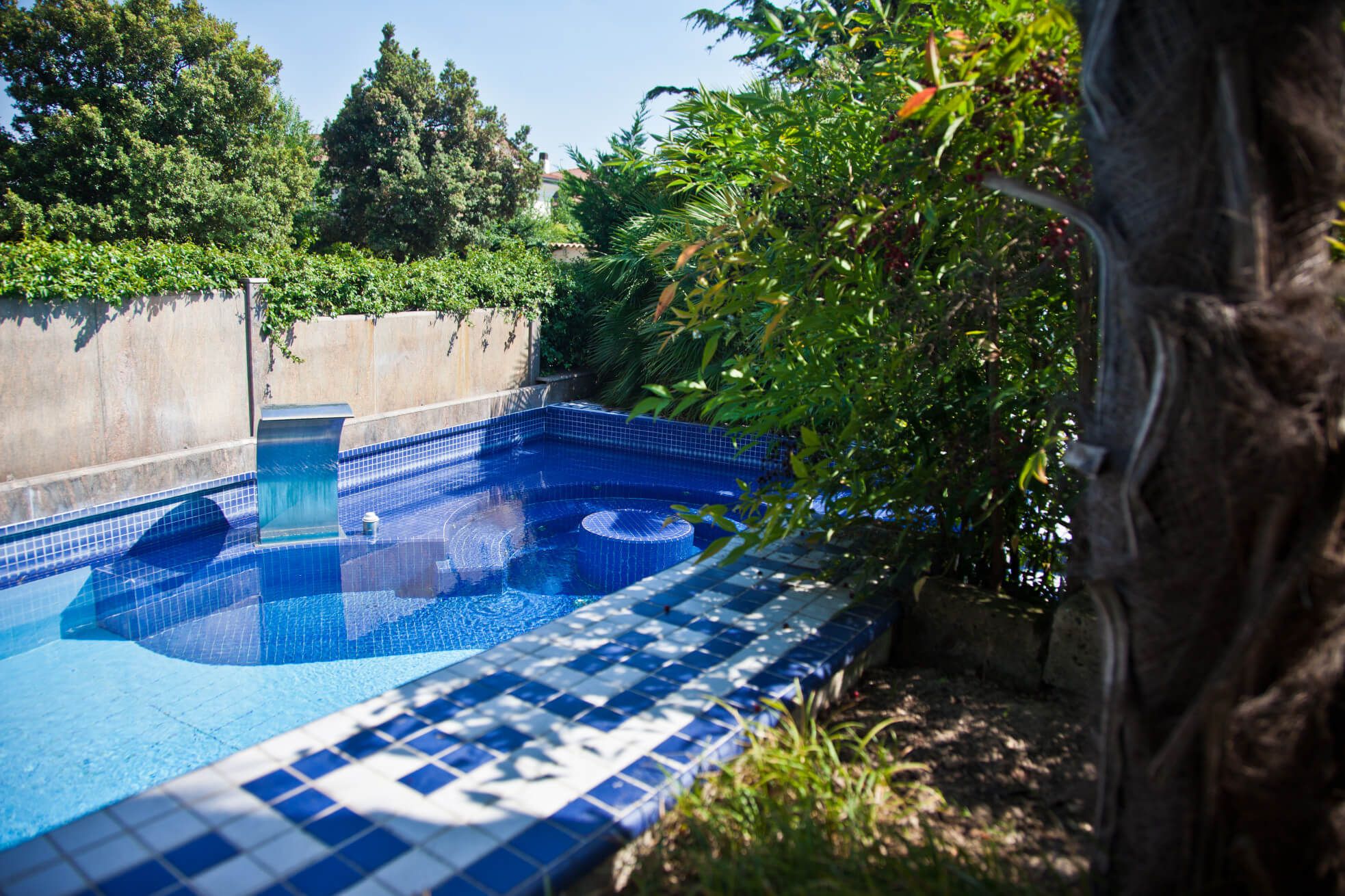 Ein blauer Pool umgeben von grünen Pflanzen und einem sonnigen Himmel, ideal zum Entspannen im Freien.