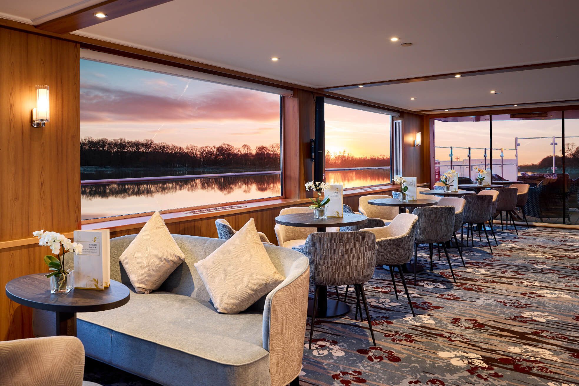 Eine elegante Lounge mit Blick auf einen ruhigen Fluss und einen beeindruckenden Sonnenuntergang durch große Fenster.