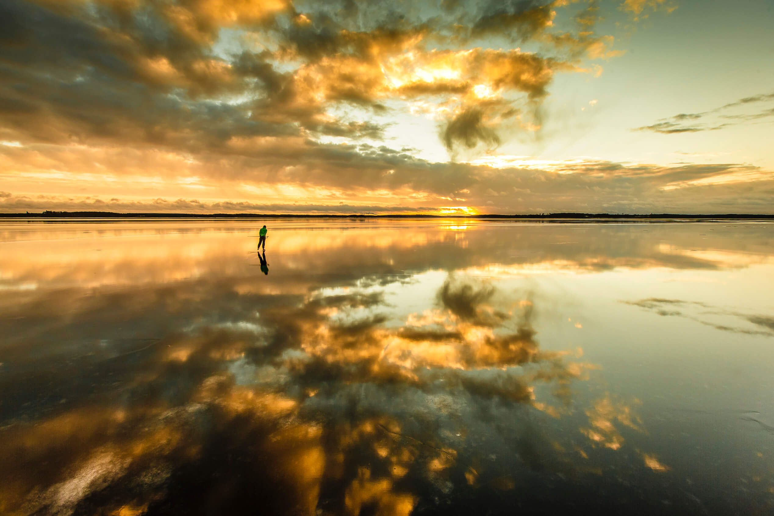 Ein Mensch steht allein auf einer spiegelnden Wasserfläche, während die Sonne hinter den Wolken untergeht.