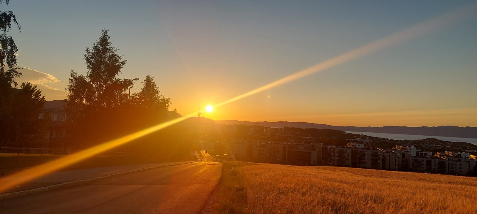 Sonnenuntergang über einer Stadt, goldene Strahlen brechen durch die Landschaft, ruhige Atmosphäre und sanfte Farben.