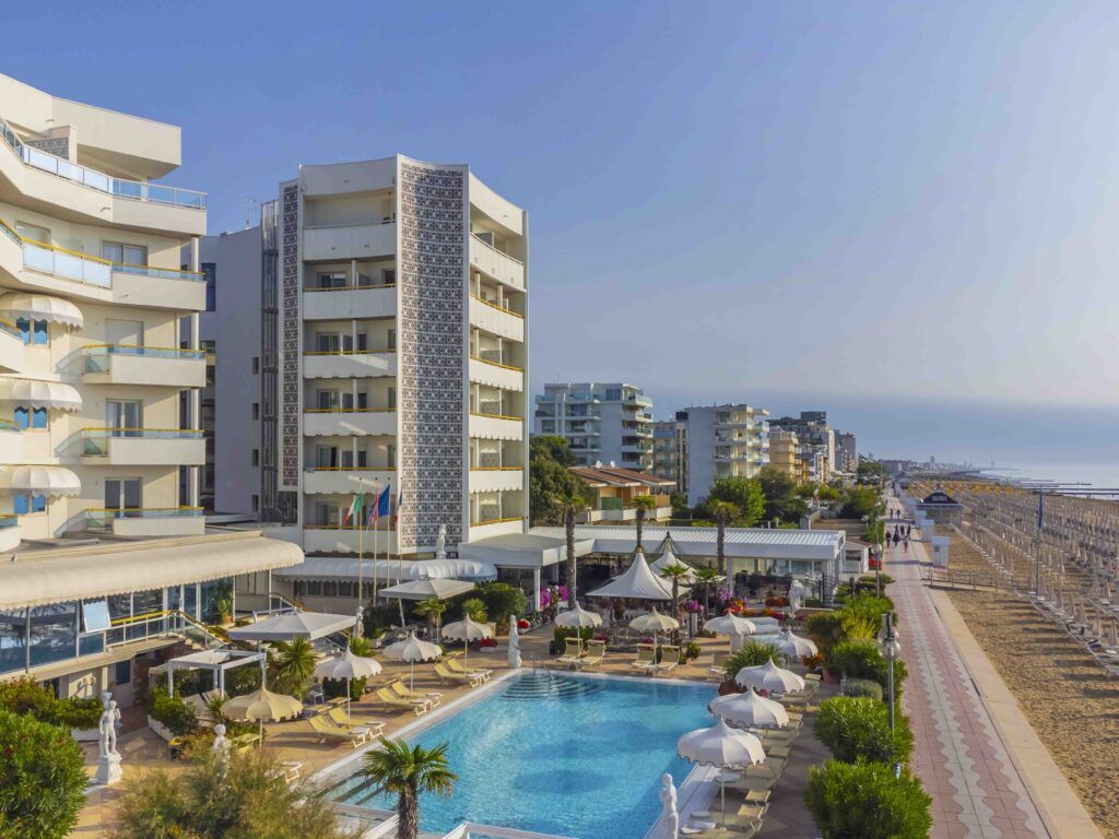 Ein Blick auf ein Hotel mit Pool, Palmen und der Strandpromenade im Hintergrund unter klarem Himmel.