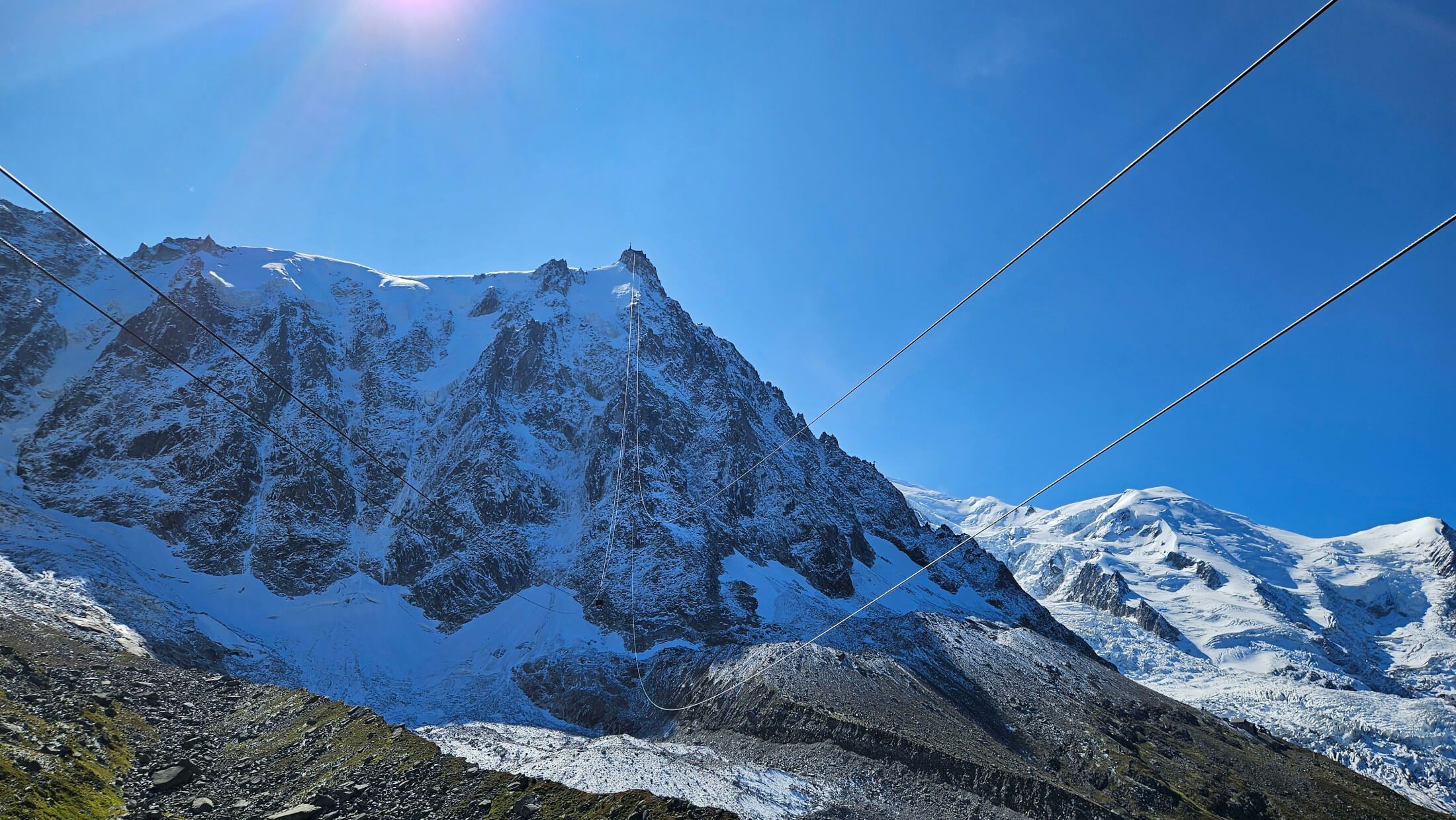 Majestätische, schneebedeckte Berge unter klarem blauem Himmel mit Seilbahnkabeln im Vordergrund.