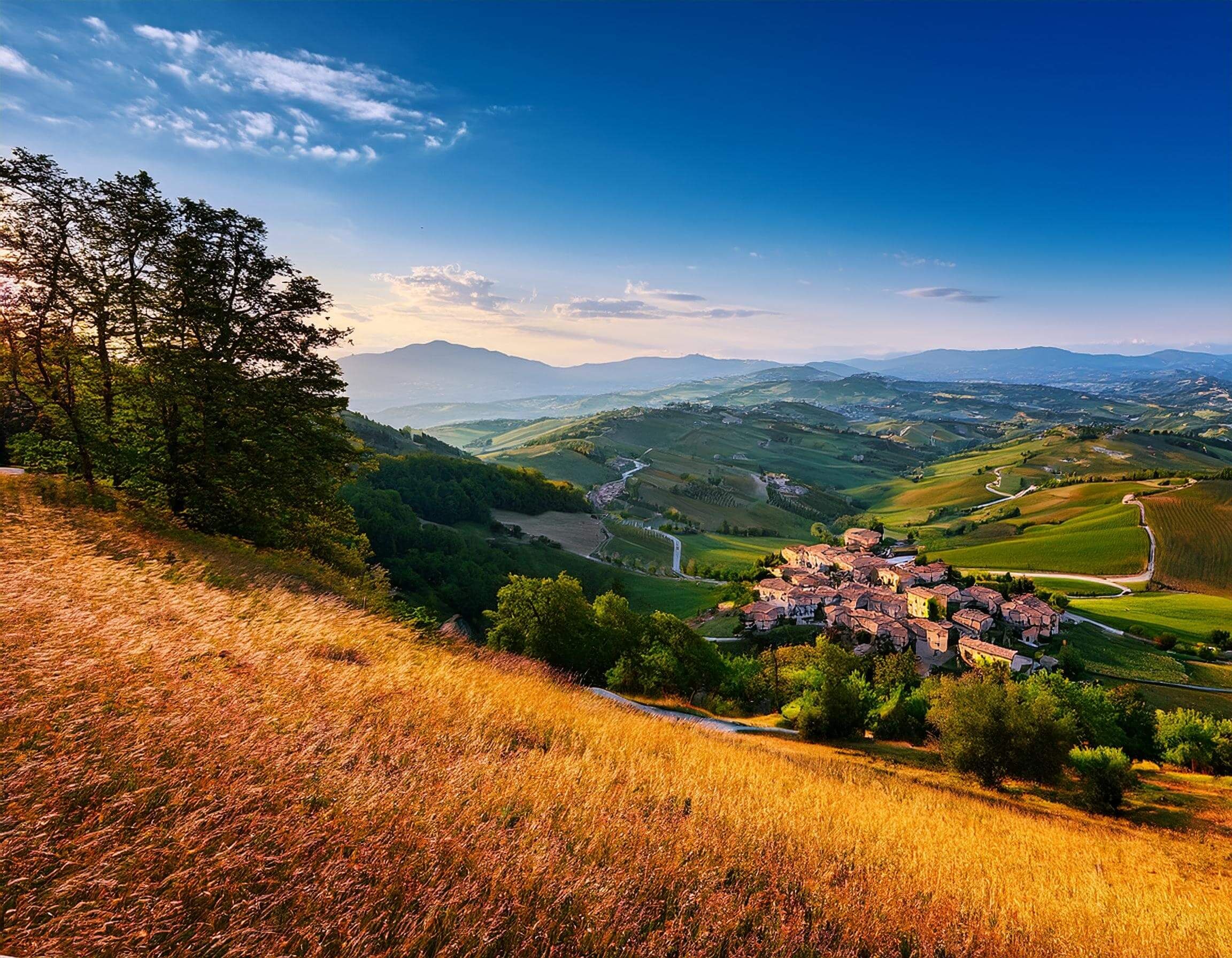 Eine malerische Landschaft mit sanften Hügeln, Weinbergen und einem kleinen Dorf unter blauem Himmel.