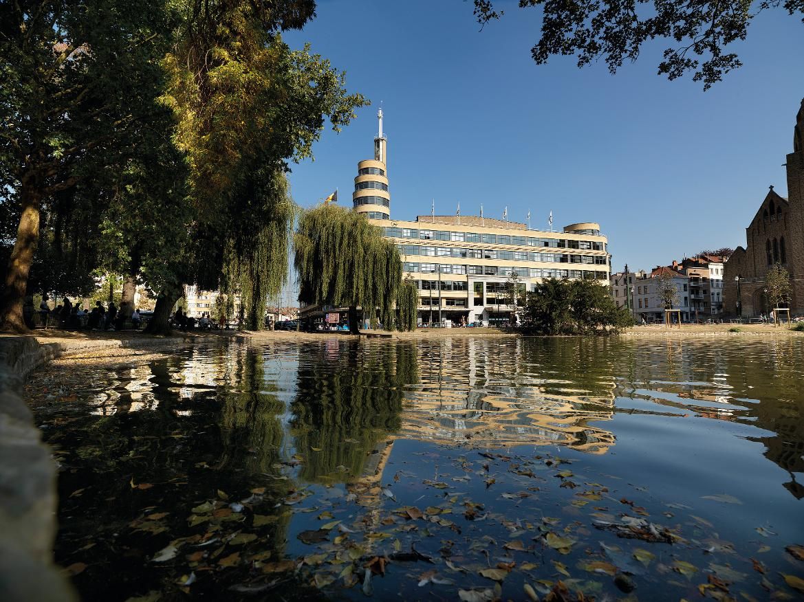 Ein ruhiger Stadtpark mit einem Spiegelbild des modernen Gebäudes und bunten Blättern im Wasser.