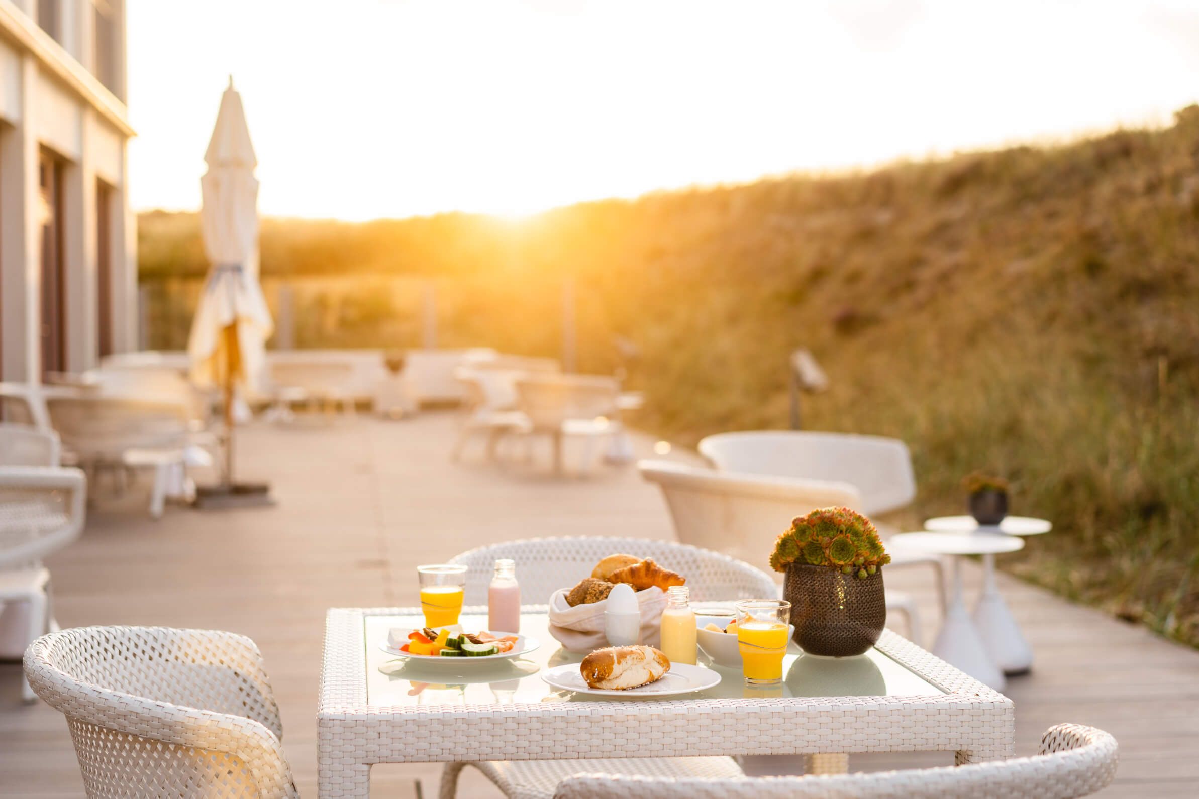 Ein schöner Tisch im Freien, mit Frühstück und Getränken, während die Sonne untergeht. Entspanntes Ambiente.