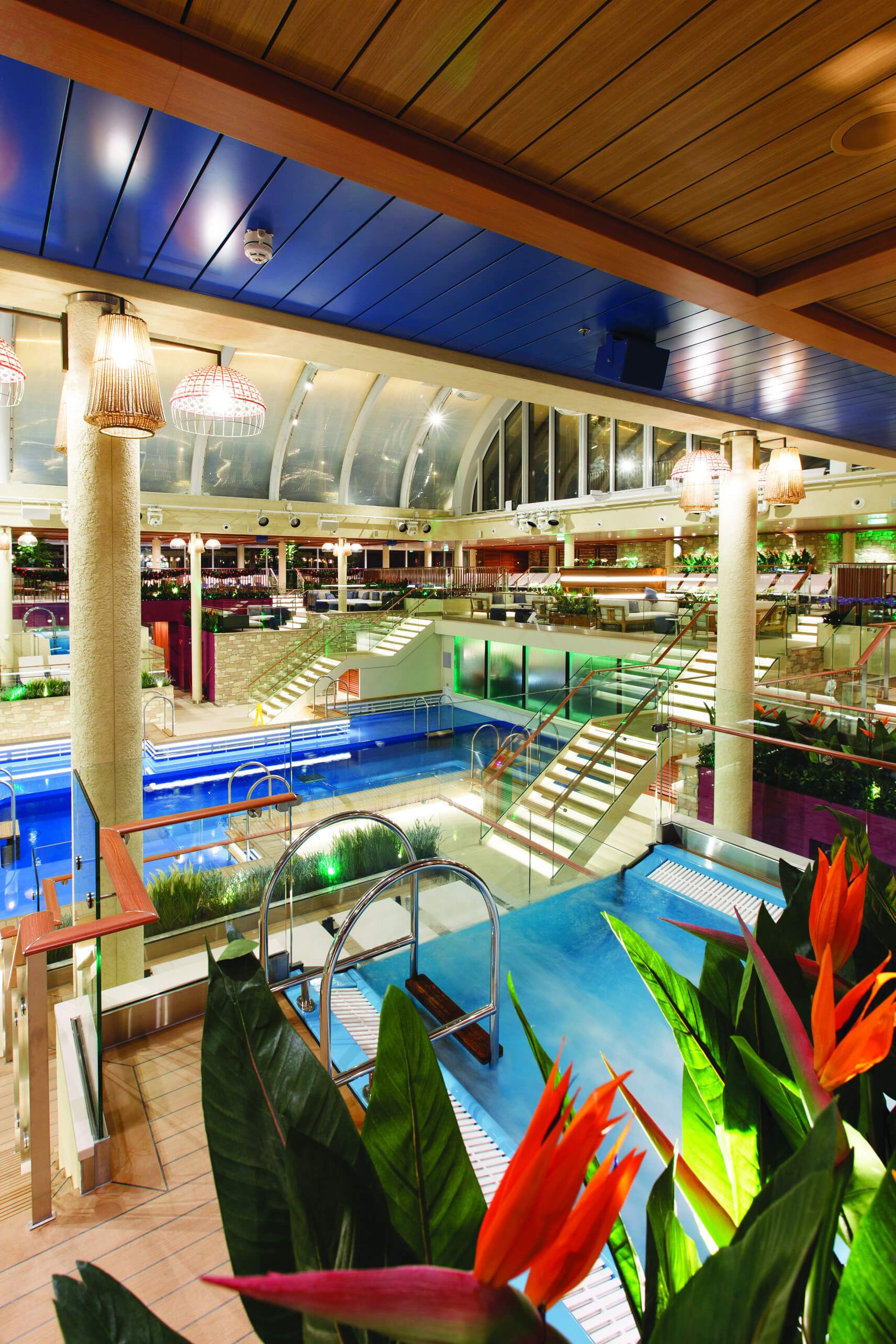 Ein modernes Schwimmbad mit mehreren Ebenen, Pflanzen und einer Glasdecke, die ein einladendes Ambiente schafft.