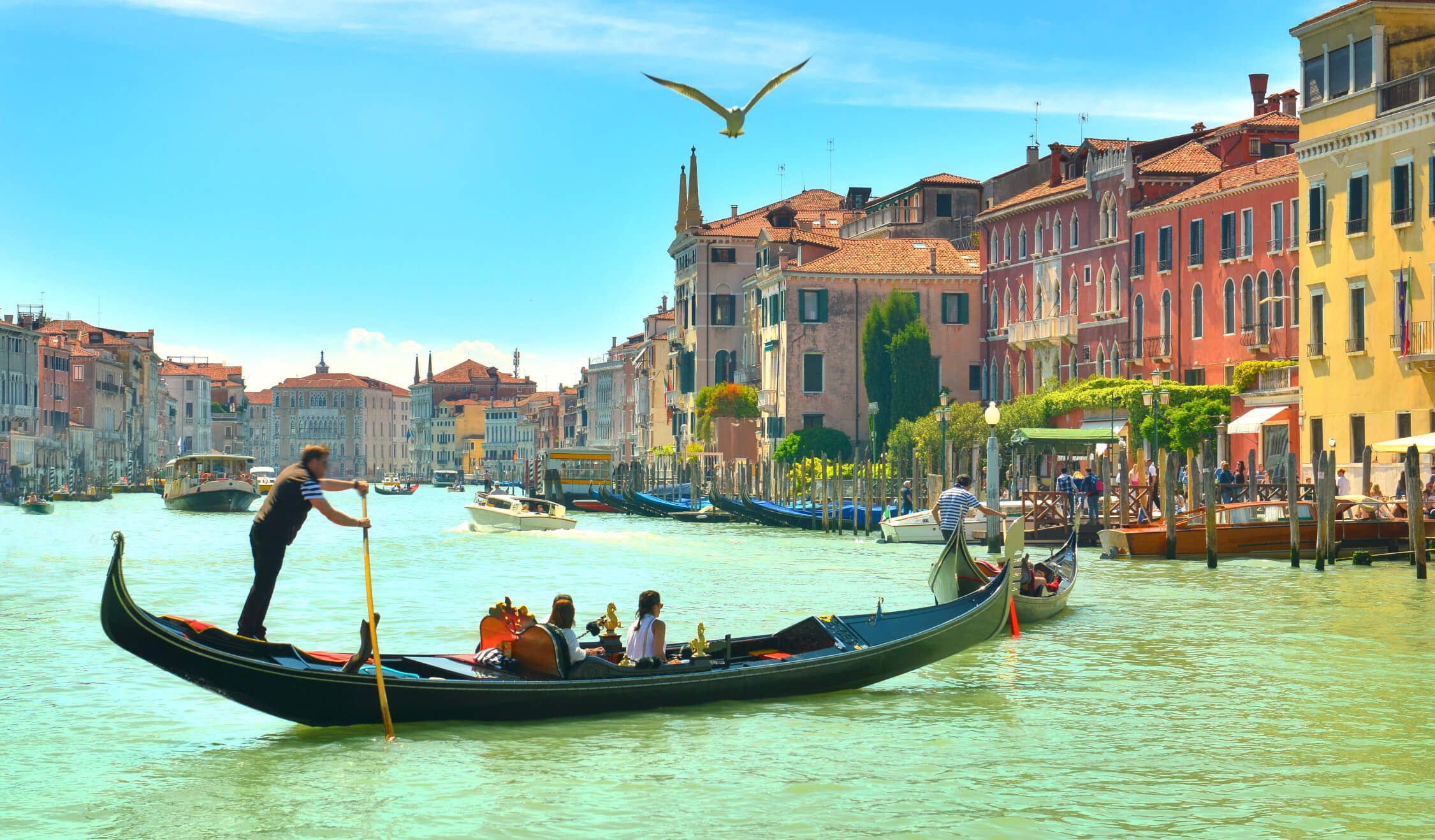 Eine sonnige Szene in Venedig mit Gondeln, bunten Häusern und Menschen am Kanal. Ein schön idyllisches Bild.